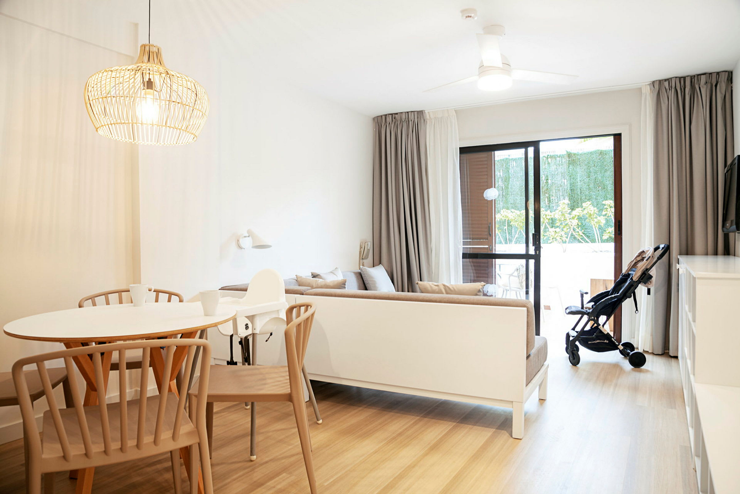 En lys og moderne innredet stue med et spisebord, en sofa og en barnevogn ved glassdøren. (AI-generert tekst)