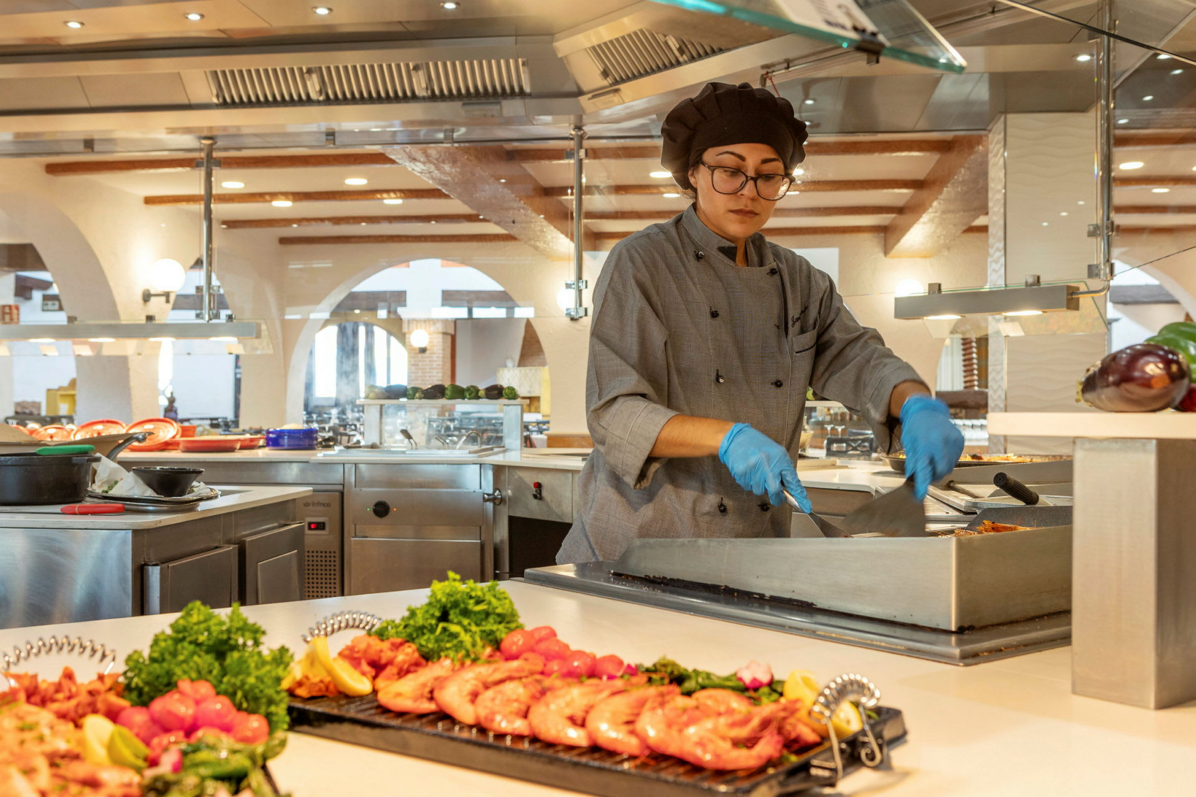En kokk tilbereder mat ved en buffetstasjon i et moderne kjøkken med hauger av ferske ingredienser. (AI-generert tekst)