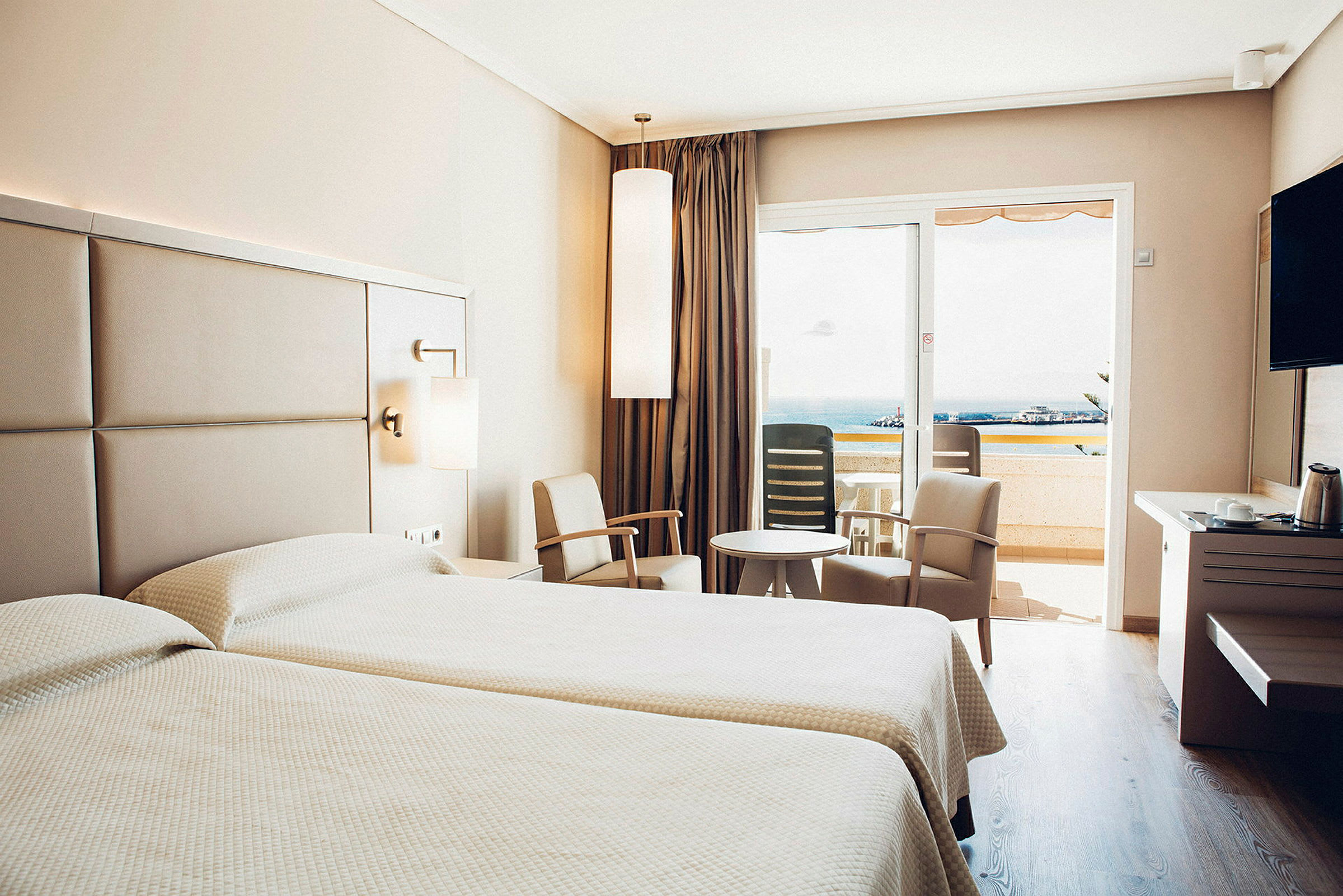 Hotellrom med to senger, sittegruppe og balkong med utsikt. (AI-generert tekst)