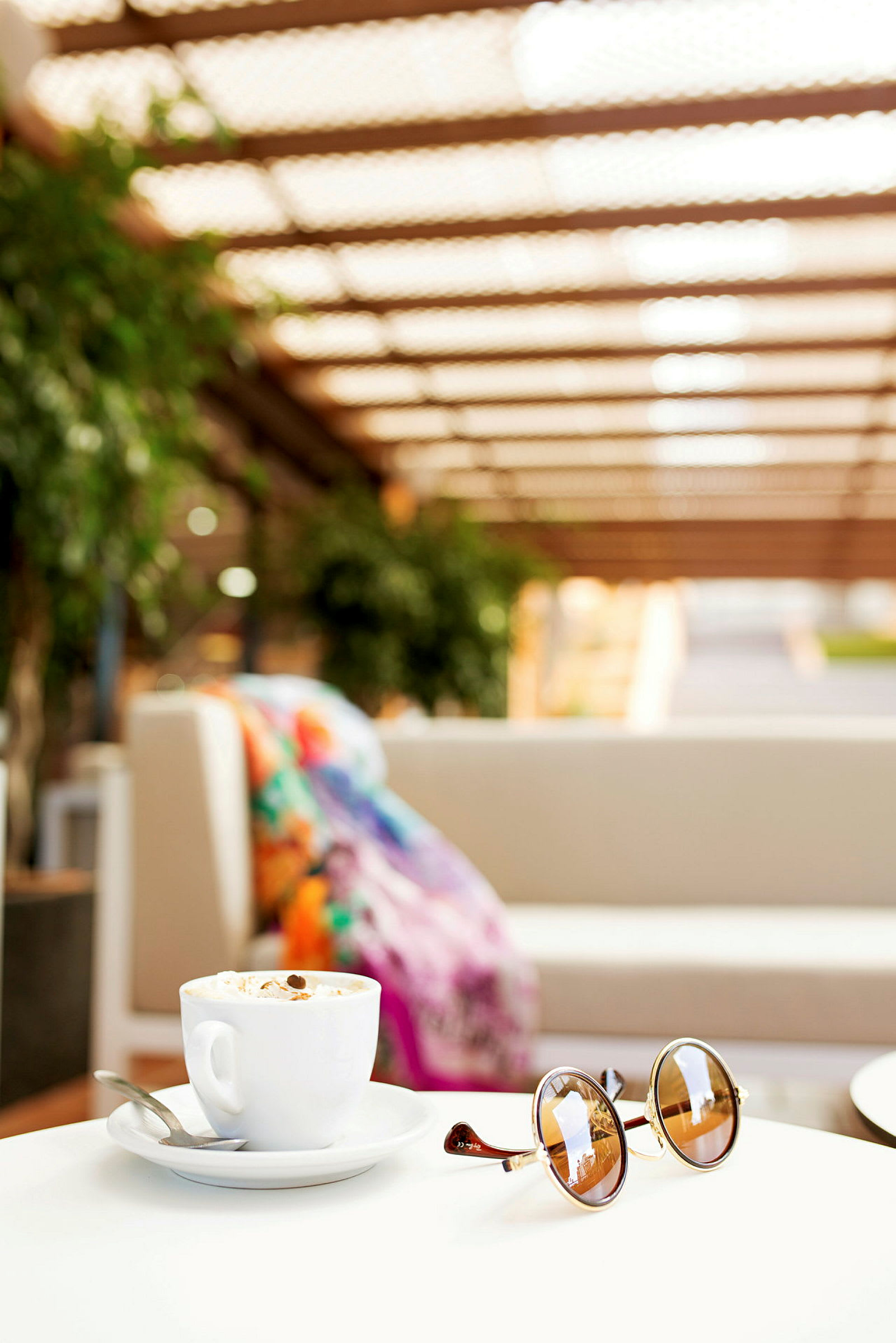 En kopp kaffe og solbriller på et bord med en sofa i bakgrunnen. (AI-generert tekst)