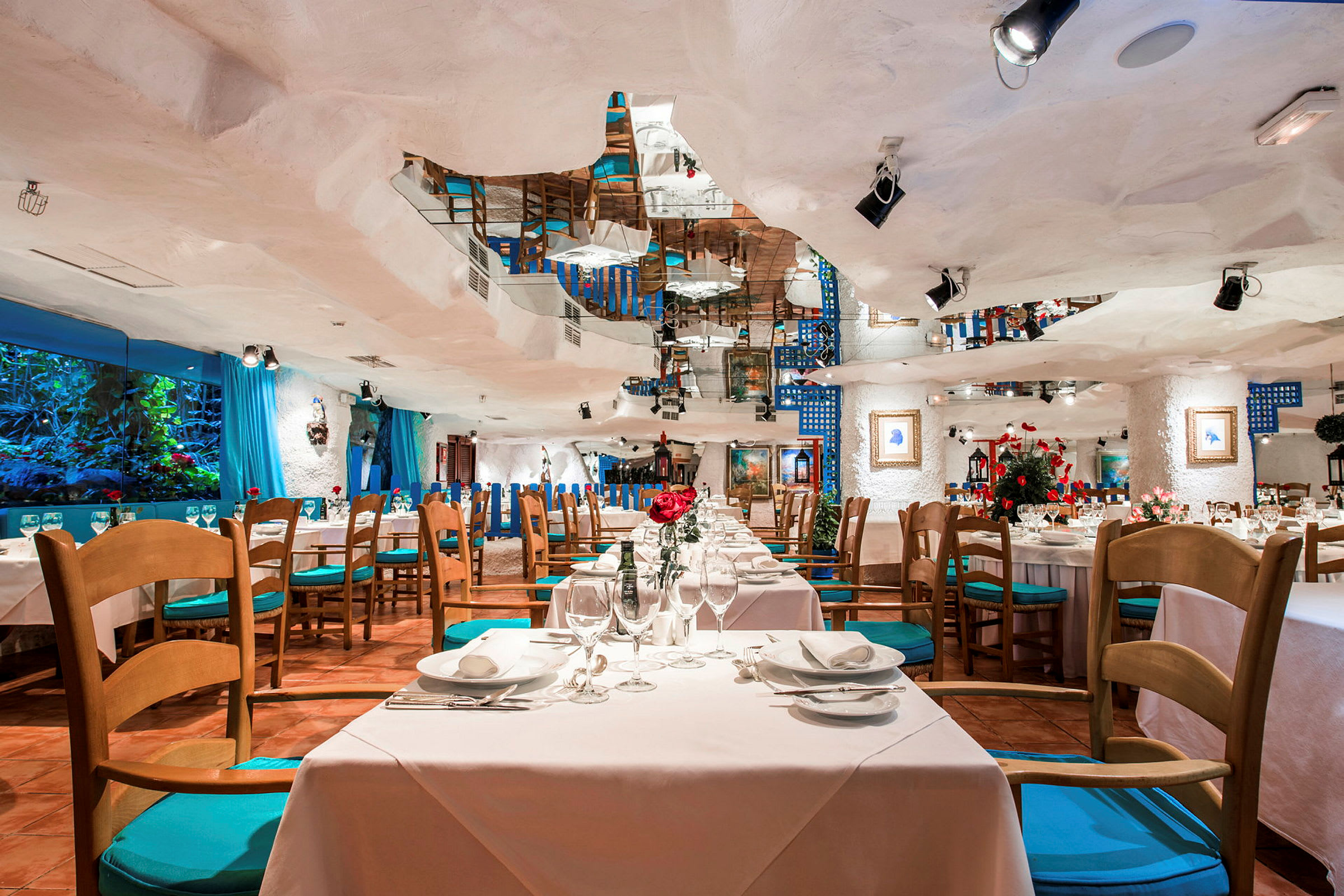 Interiøret til en restaurant med bord og stoler, dekorert med blomster og speil. (AI-generert tekst)