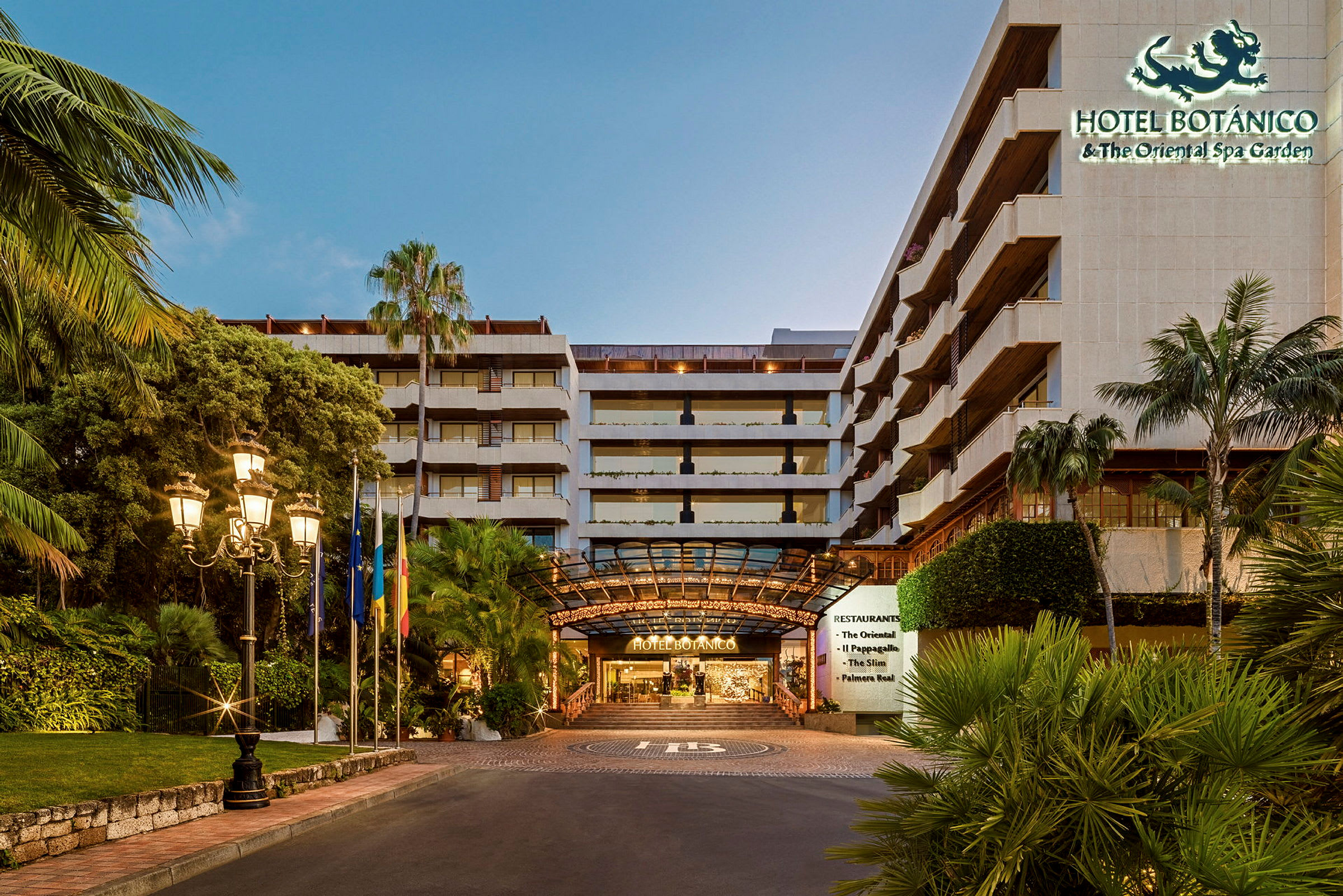 Inngangen til Hotel Botanico, omgitt av tropiske planter og opplyst av gatelys. (AI-generert tekst)