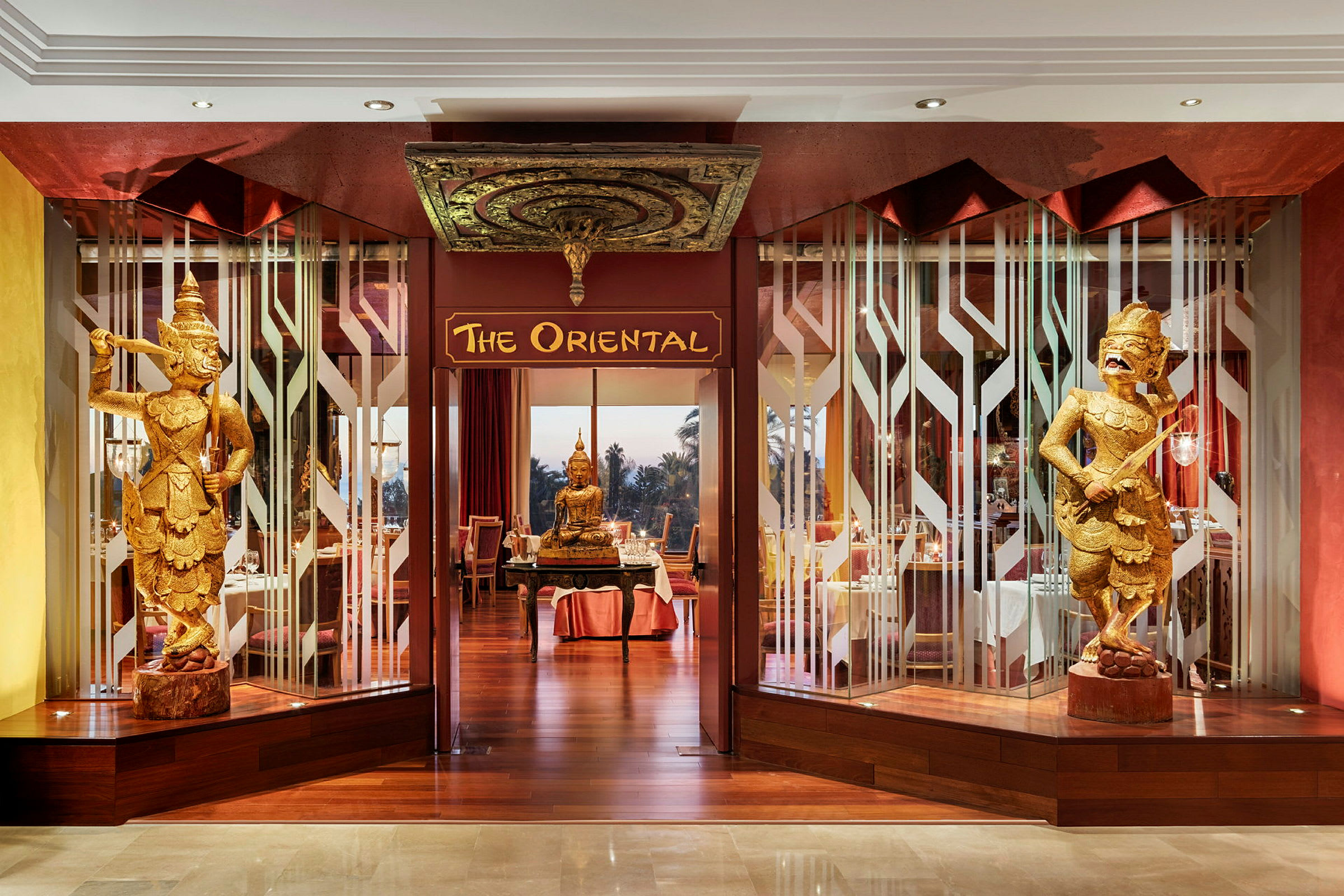 Inngangen til restauranten 'The Oriental' med dekorative gyldne figurer og en Buddha-statue. (AI-generert tekst)