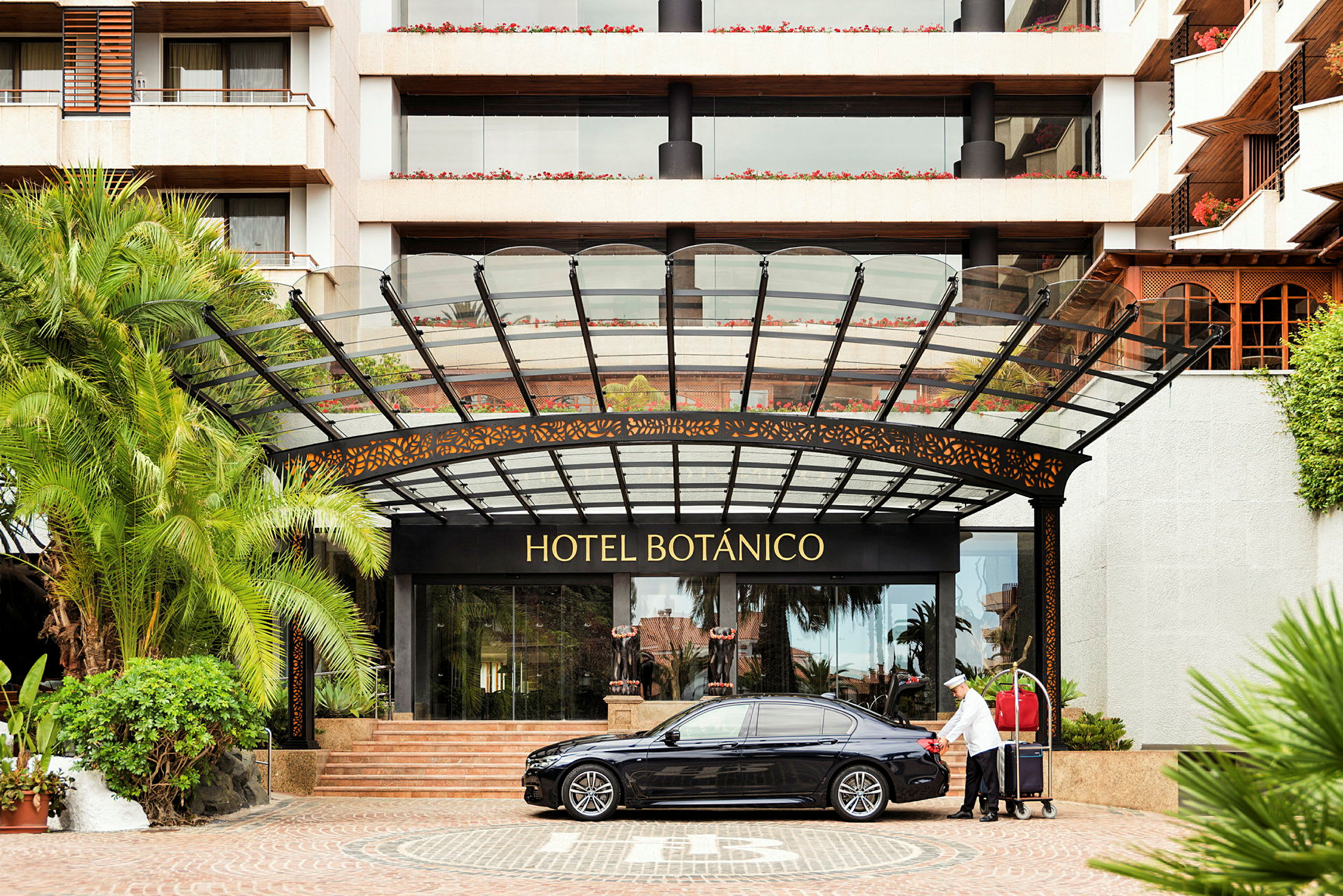 Inngangen til Hotel Botánico med en bil og en bagasjetralle. (AI-generert tekst)