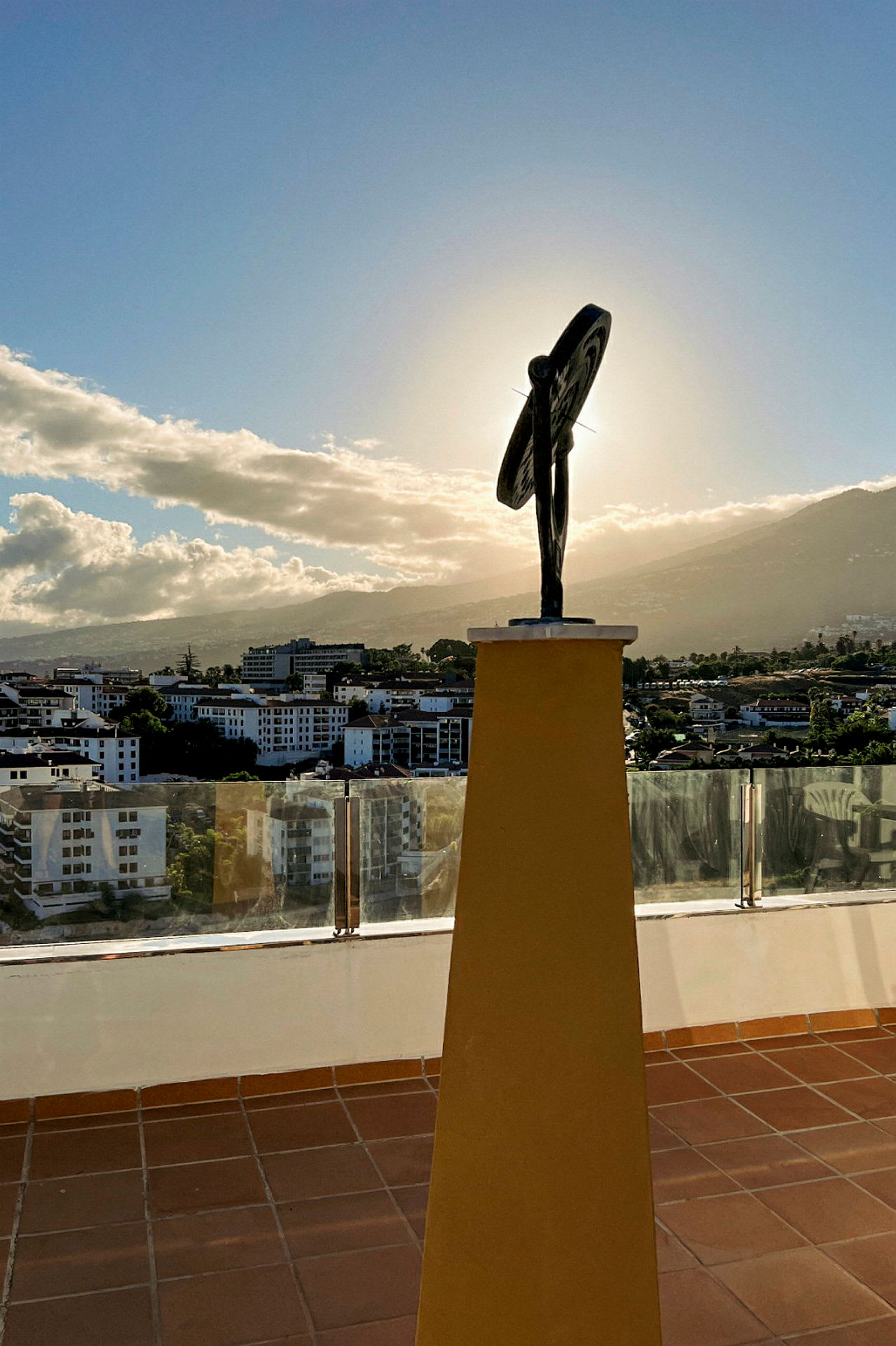 En skulptur på en gul sokkel med en by og fjell i bakgrunnen. (AI-generert tekst)