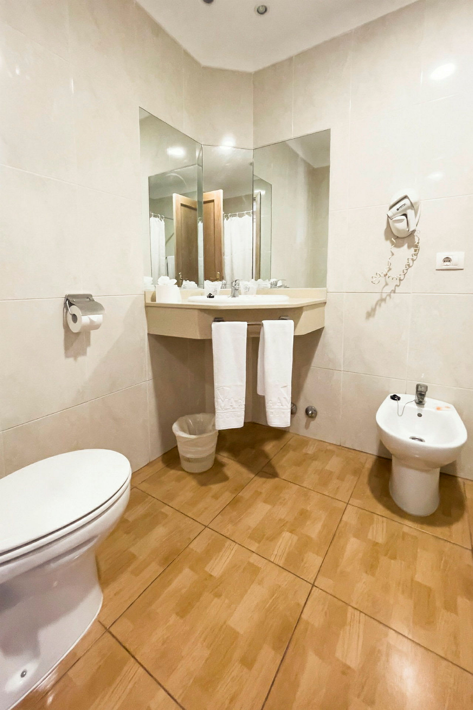 Bad med toalett, bidet, servant med speil og håndklær. (AI-generert tekst)