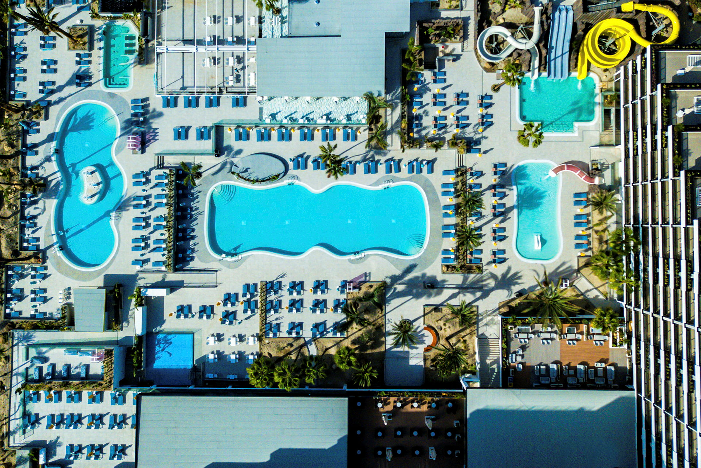 Flere bassenger og solsenger sett ovenfra på en resort. (AI-generert tekst)
