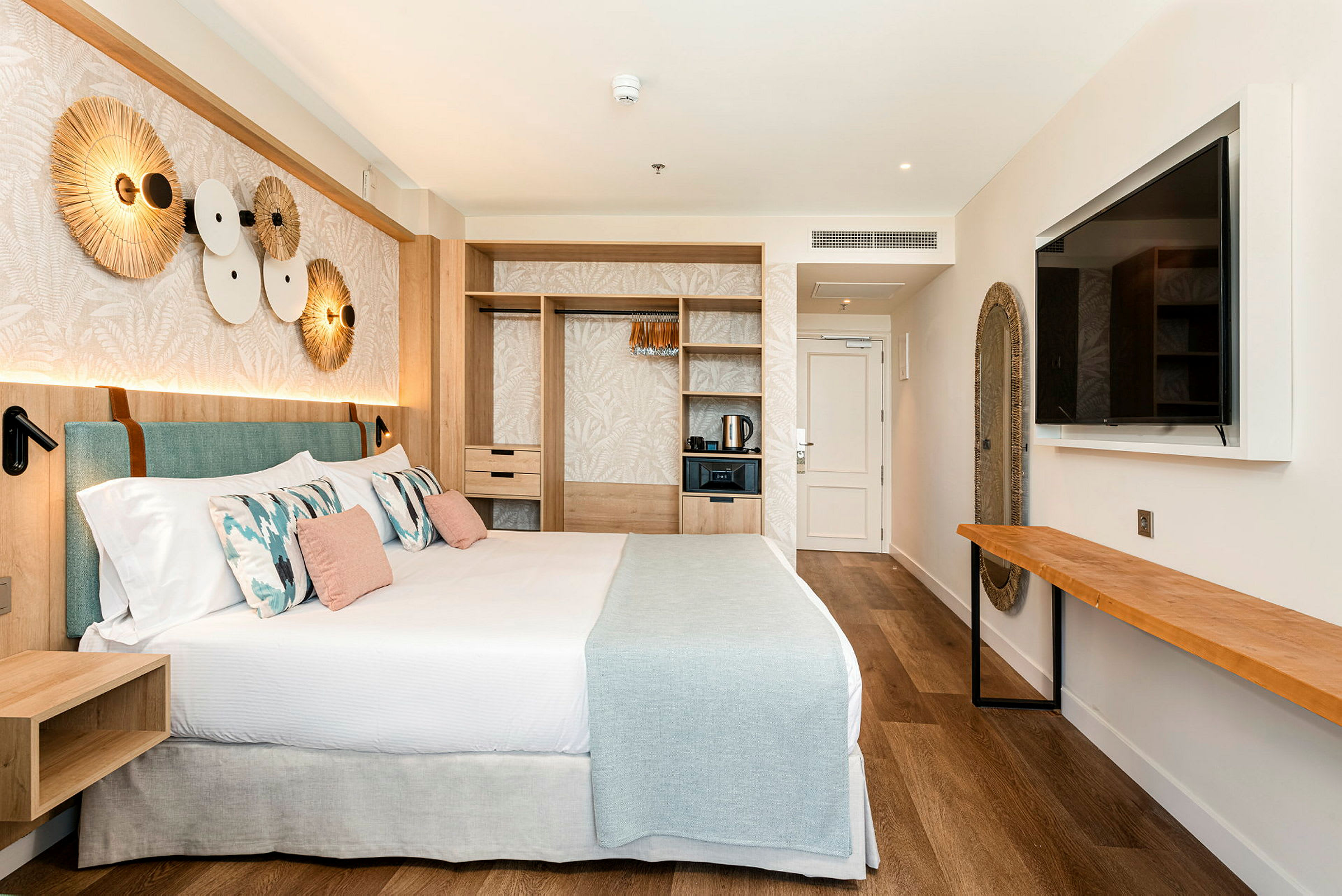Et moderne hotellrom med en stor seng, innredning i lyse farger og designdetaljer, inkludert en veggdekorasjon og en stor veggmontert TV. (AI-generert tekst)