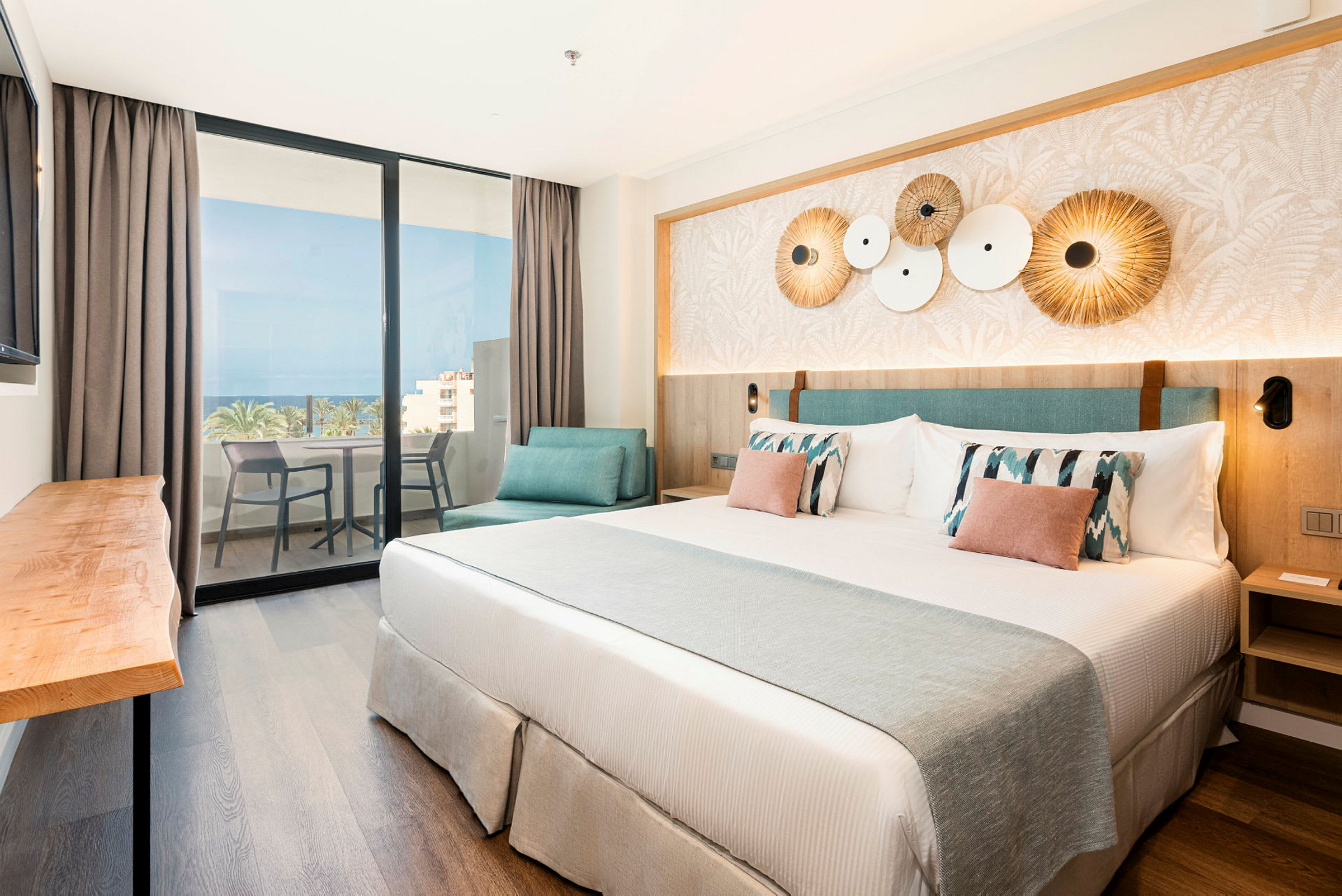 Et hotellrom med en dobbeltseng, dekorerte puter og en sitteplass. Det er en balkong med utsikt over havet. (AI-generert tekst)
