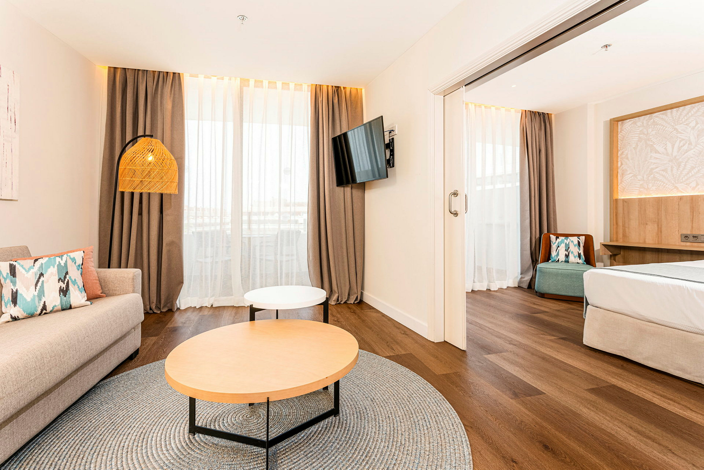 Et lyst hotellrom med en stueområde, sofa, salongbord og en TV på veggen. Sovedelen ligger ved siden av. (AI-generert tekst)