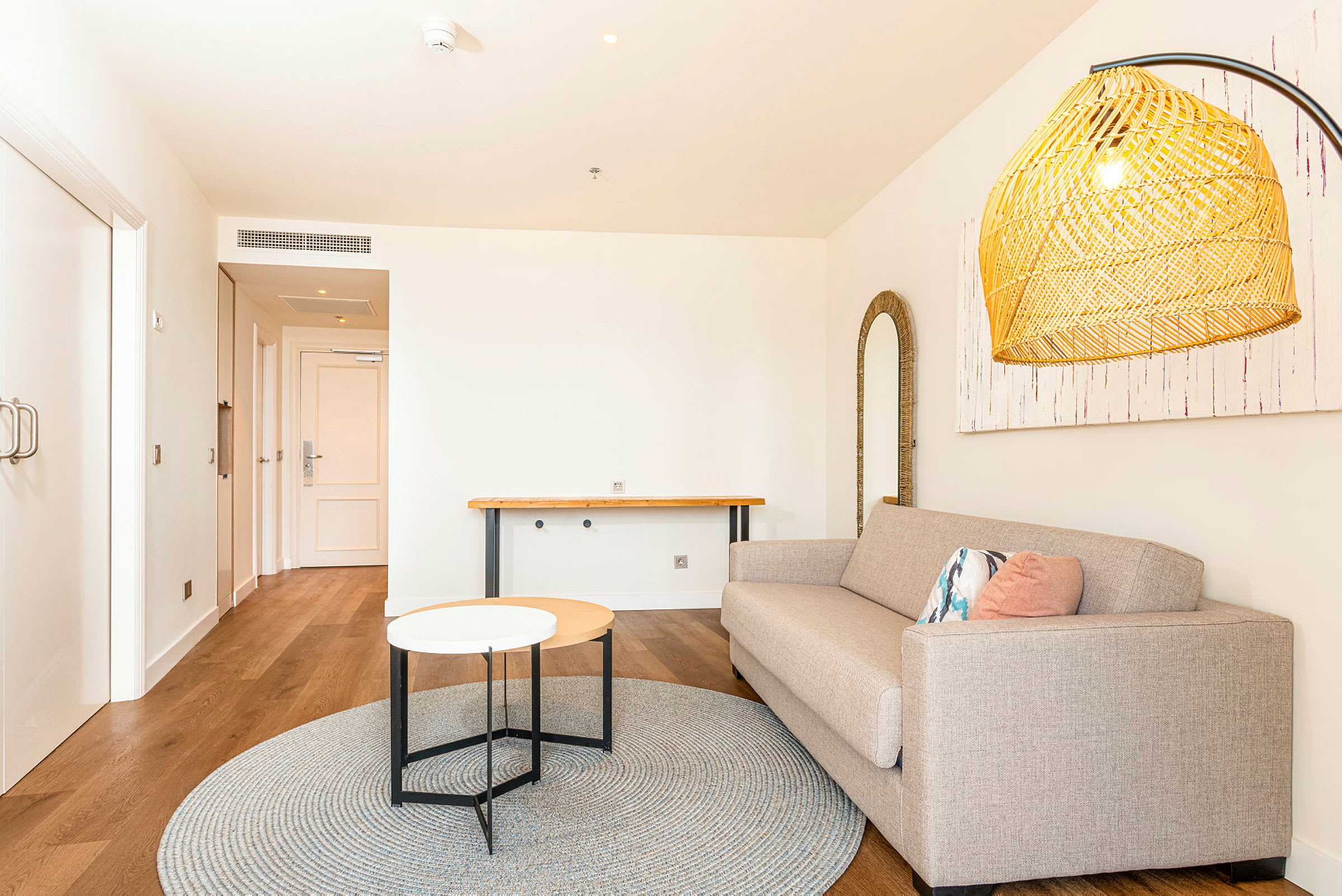 En moderne innredet interiør som viser en stue med beige sofa, lite sidebord, rund matte og en dekorativ belysning. (AI-generert tekst)