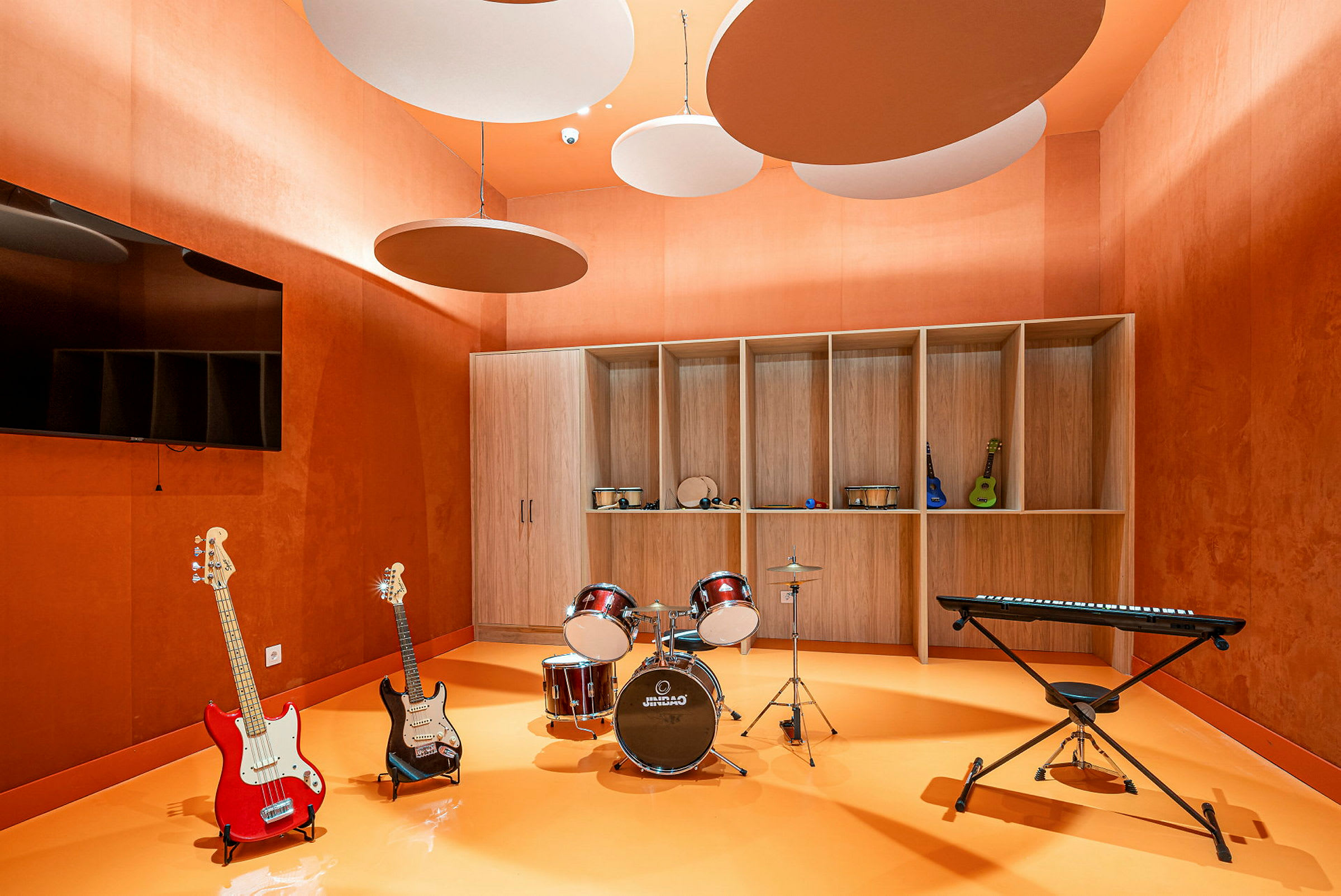 Et musikkrom med instrumenter inkludert elektriske gitarer, et trommesett og et elektronisk keyboard arrangert i et oransje rom. (AI-generert tekst)