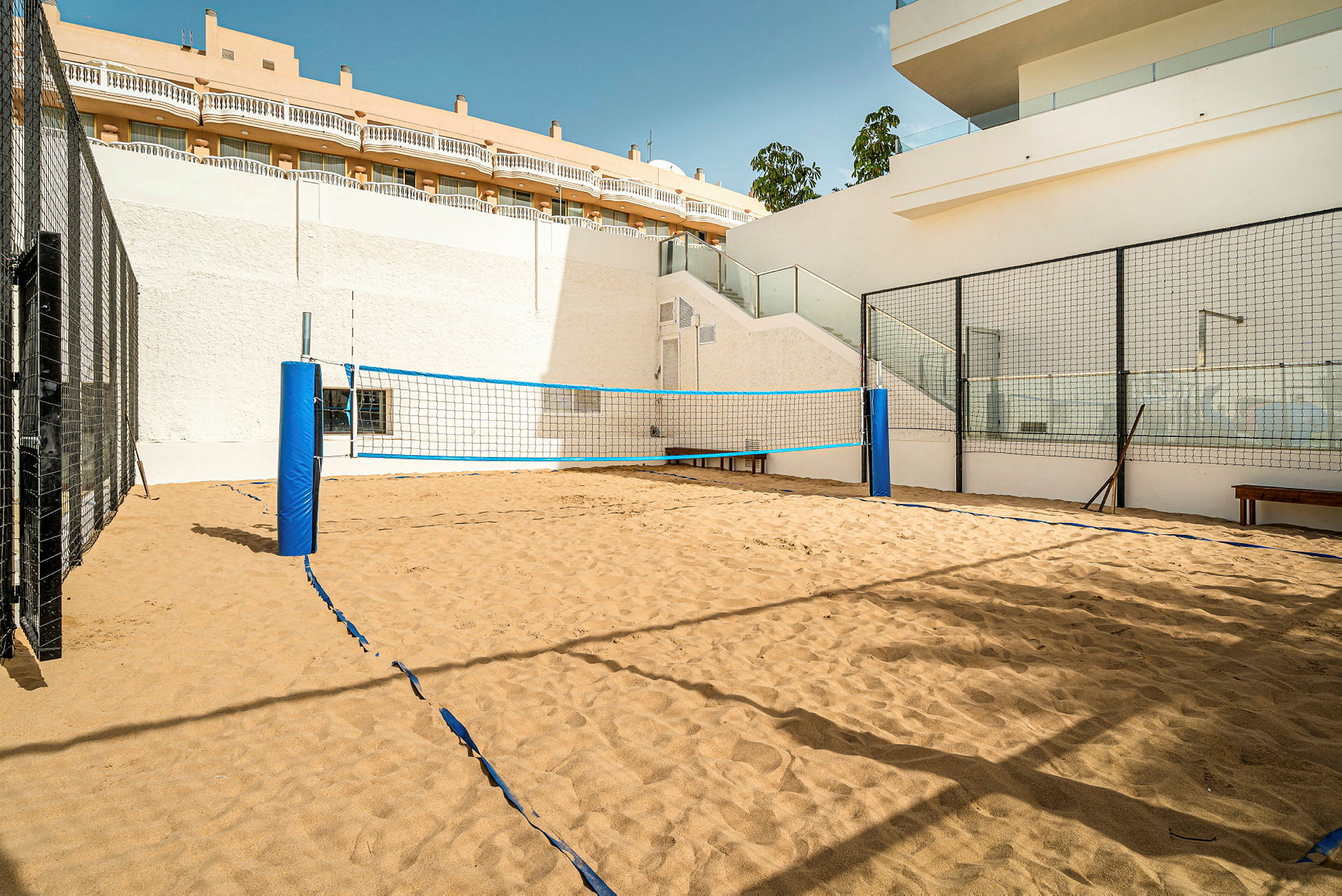 En sandvolleyballbane omgitt av gjerder og bygninger. (AI-generert tekst)