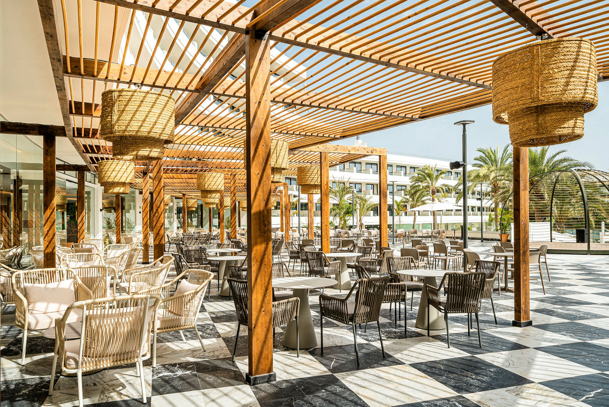 Utendørs restaurant med bord og stoler plassert under en pergola med trelister. (AI-generert tekst)