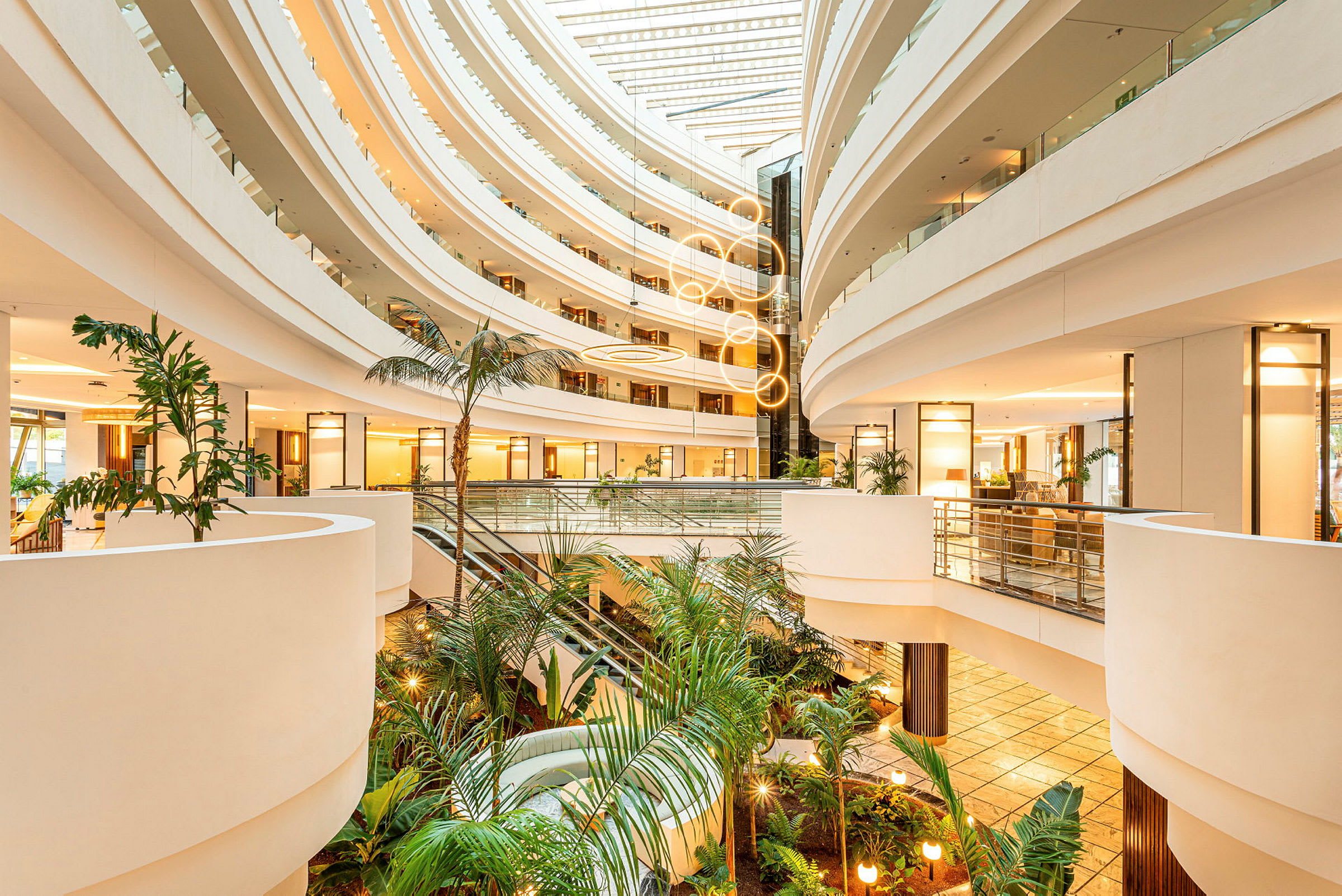 Moderne hotellatrium med flere etasjer, velplanerte gangveier, glassrekkverk og pottplanter i første etasje. (AI-generert tekst)