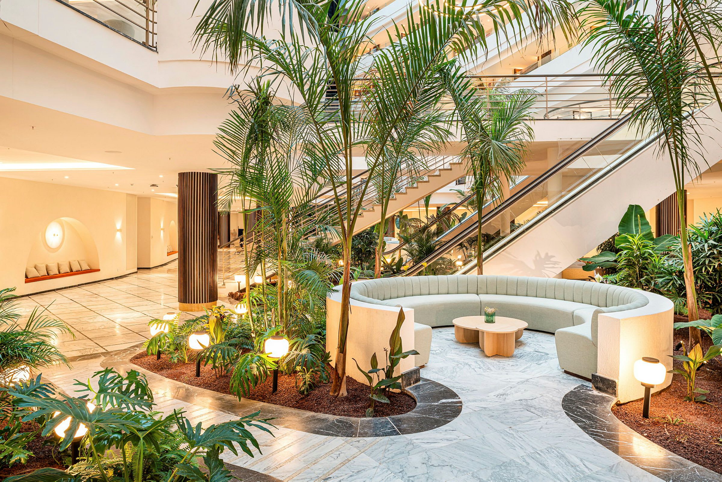 Interiørbilde av en lys og moderne hotellobby med grønne planter, sittemøbler og trapper. (AI-generert tekst)