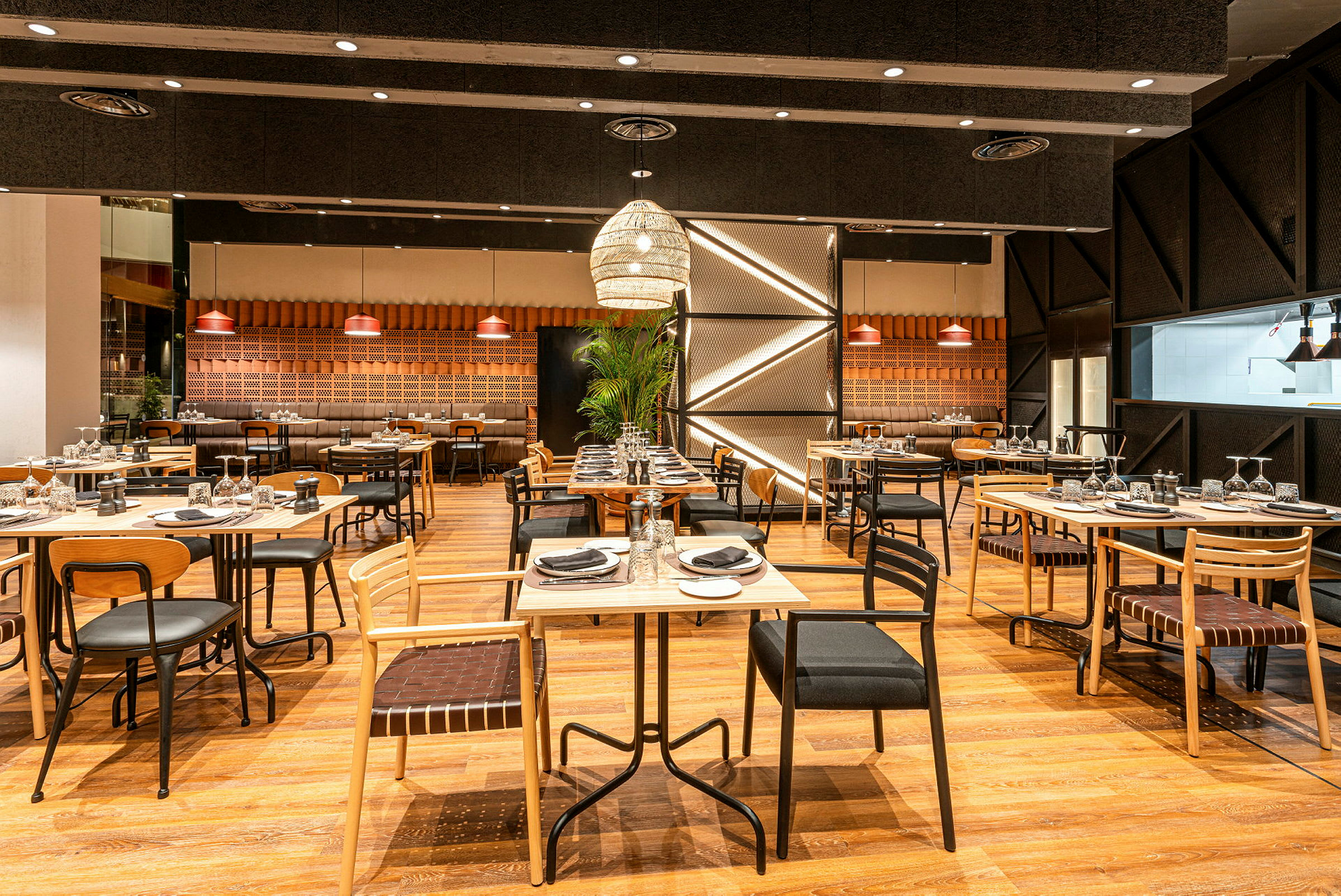 En moderne restaurant med trestoler og bord ordnet i et åpent område, dekorert med hengende lamper og grønne planter. (AI-generert tekst)