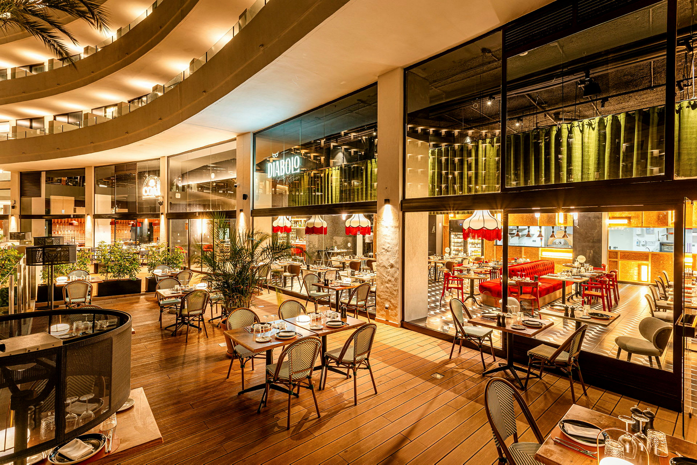 En restaurant med moderne interiør, bord og stoler på en treveranda og innendørs med fargerike detaljer. (AI-generert tekst)