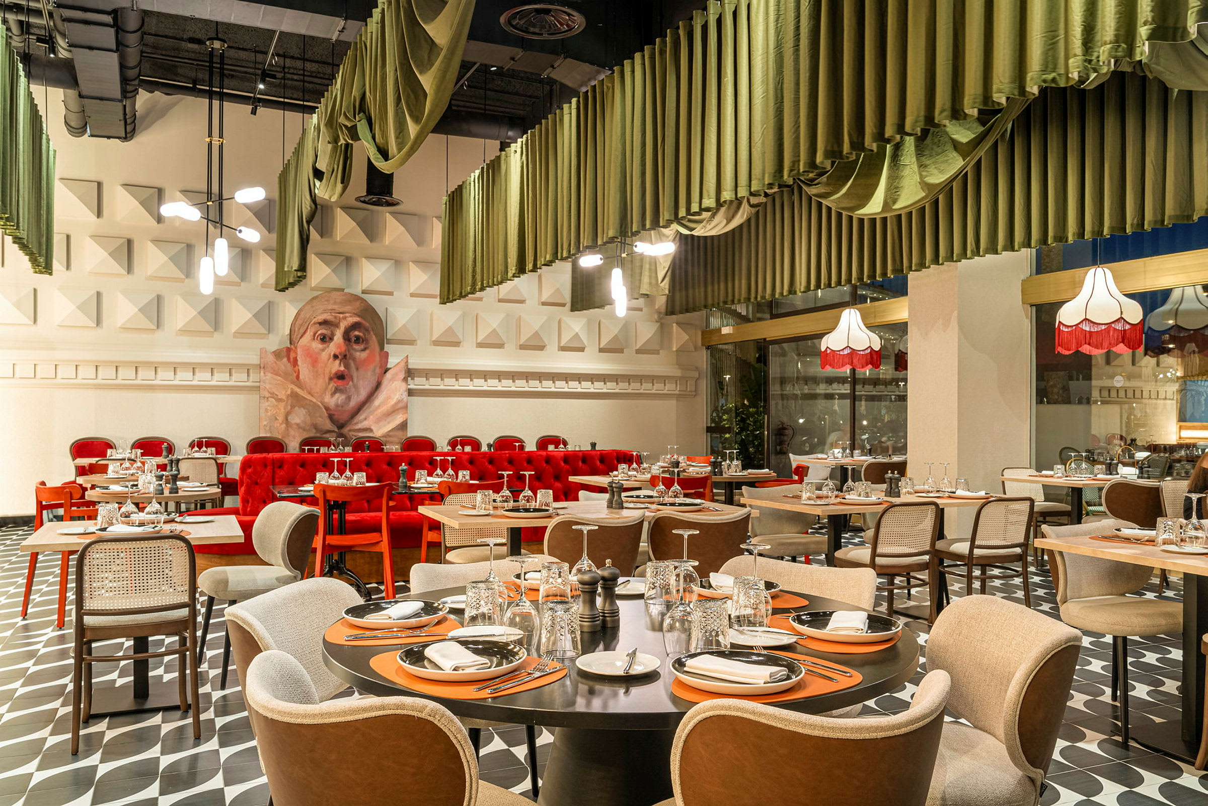 Et dekorert restaurantinteriør med dekkede bord og stoler, røde sofaer og grønne gardiner som henger i bølger fra taket. (AI-generert tekst)