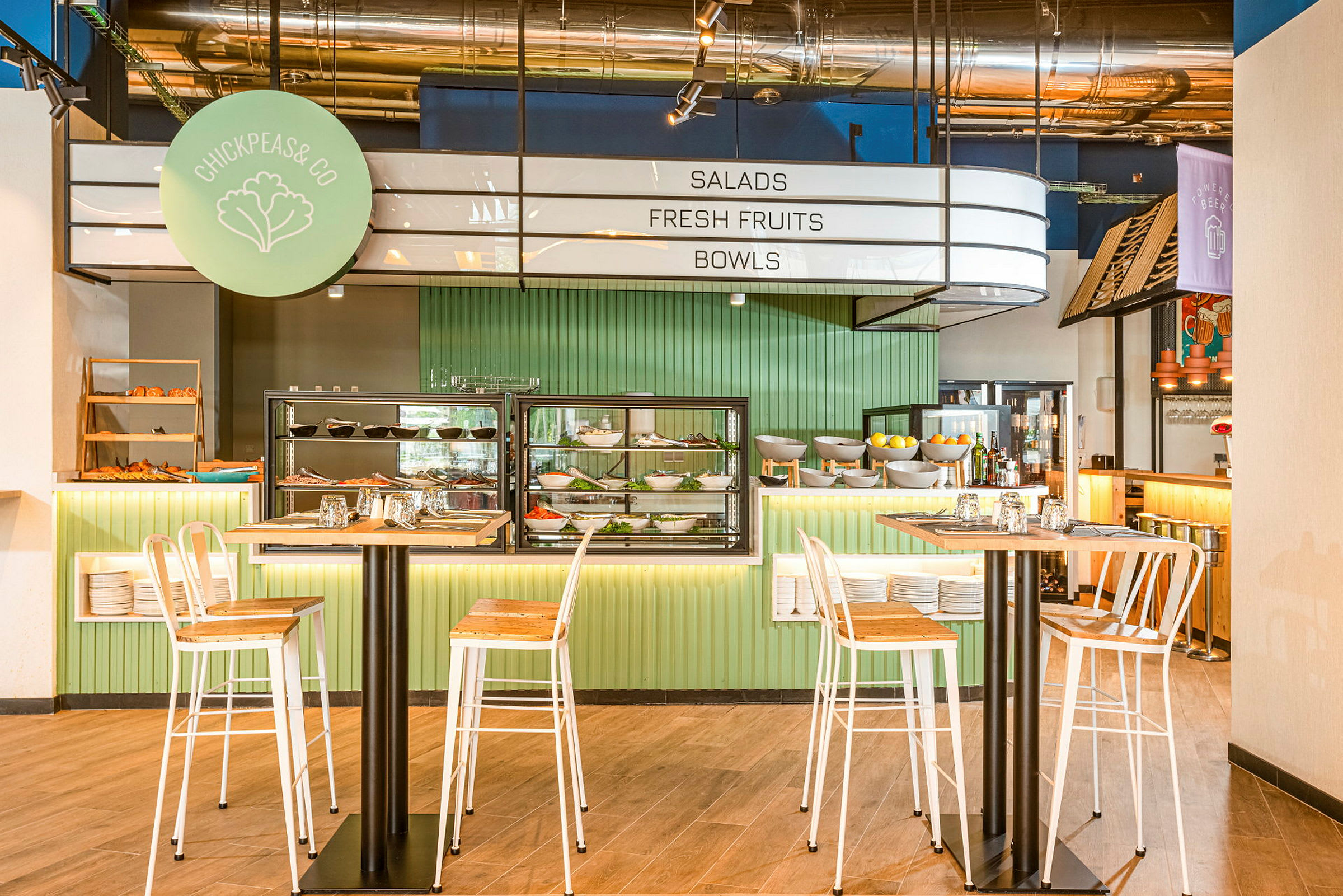 Innredningen i en moderne restaurant med høye bord og stoler foran en salat- og fruktbuffé. (AI-generert tekst)