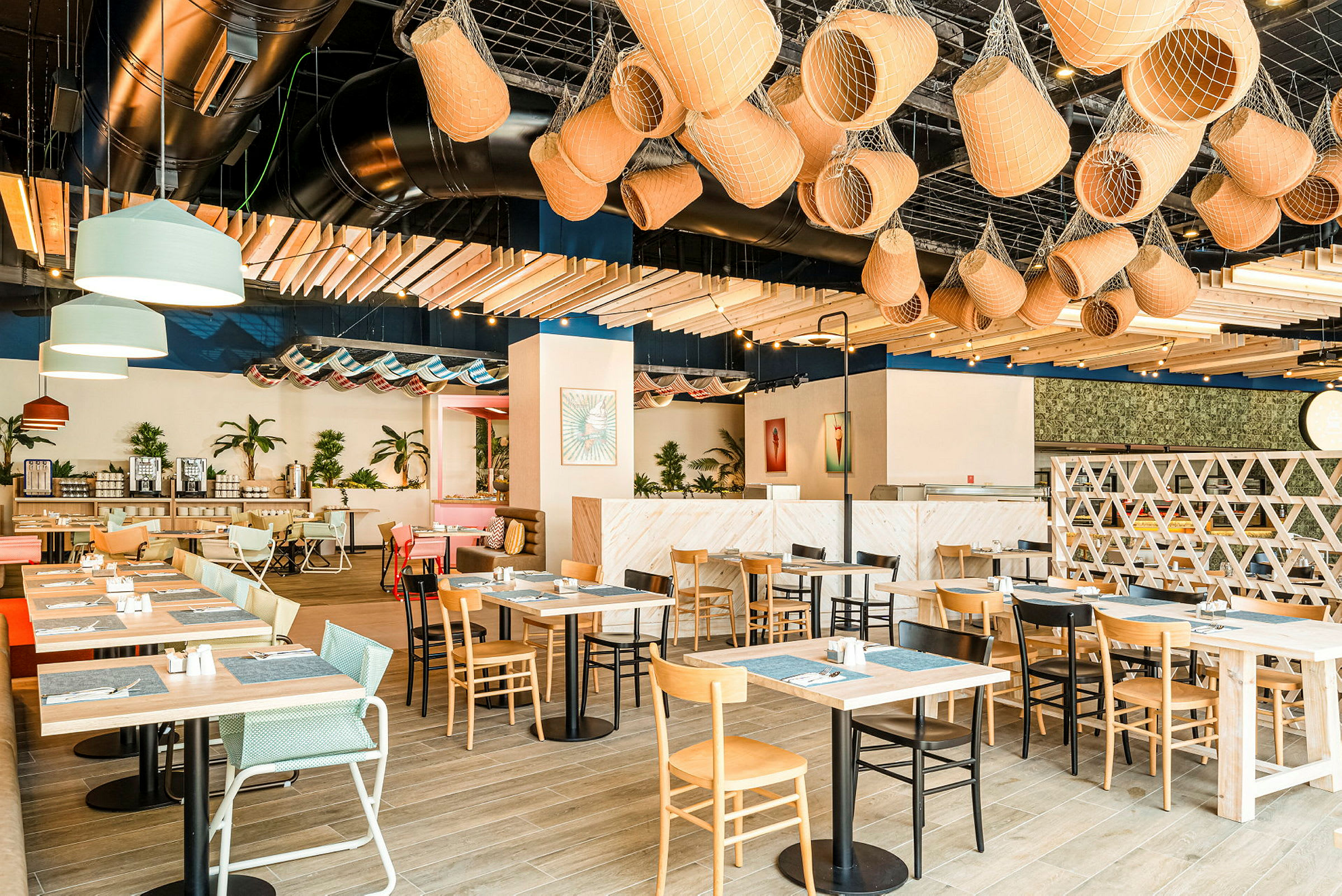 En lys og moderne restaurant med trebord, ulike typer stoler, planter og dekorative objekter i taket. (AI-generert tekst)