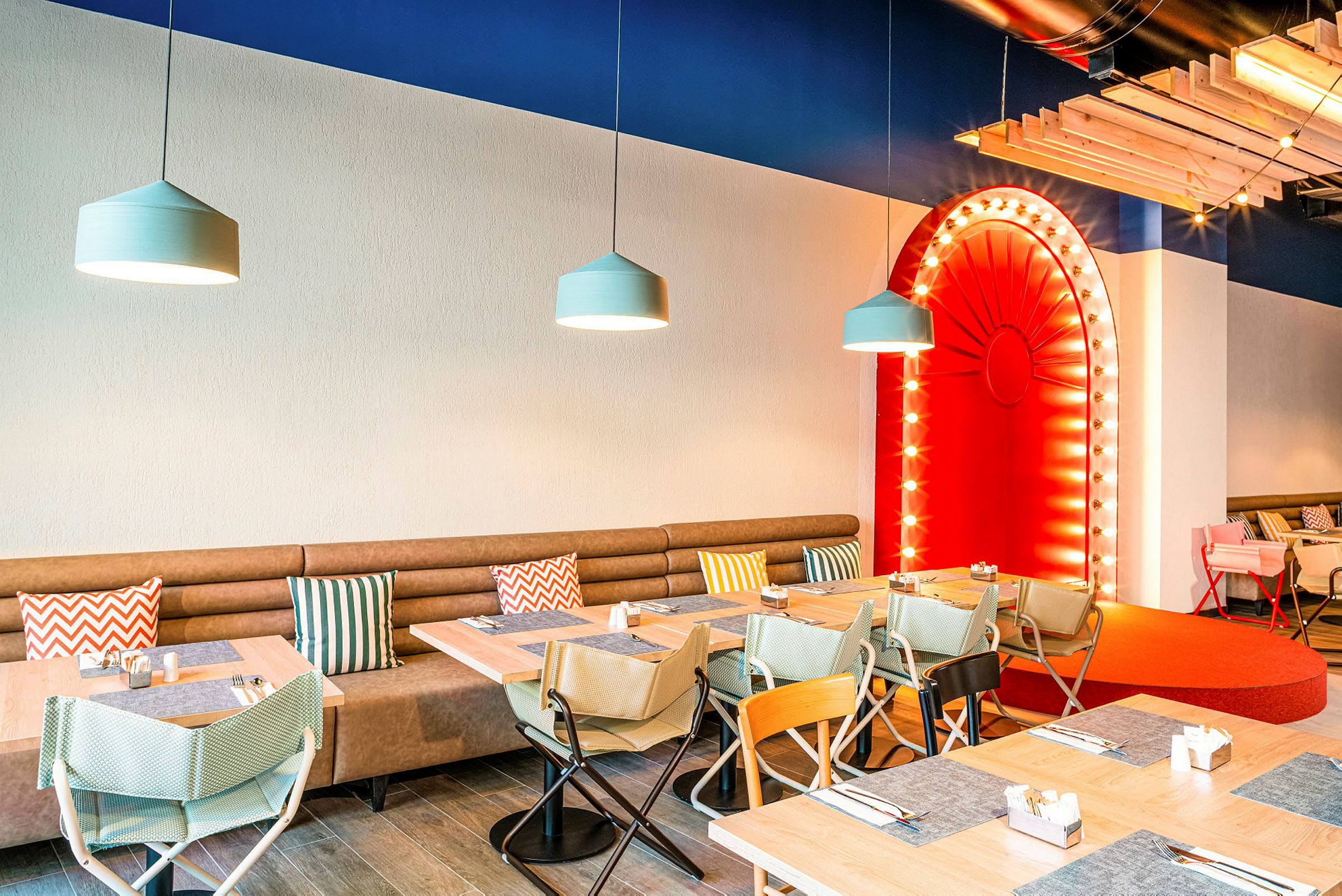 Restaurantinteriør med bord og stoler, beige sofa med fargerike puter og en rød dekorativ bue. (AI-generert tekst)