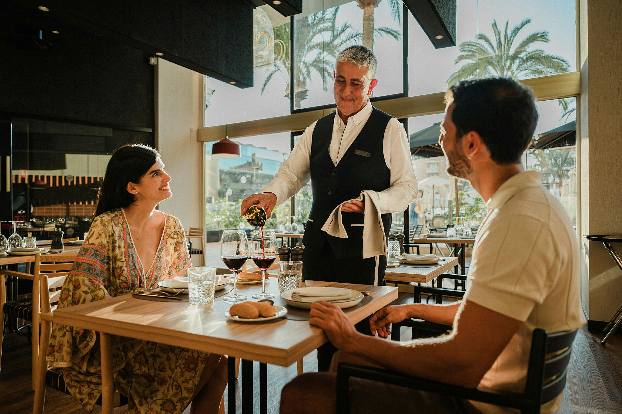 En kelner serverer vin til et par som sitter ved et bord på en restaurant. (AI-generert tekst)