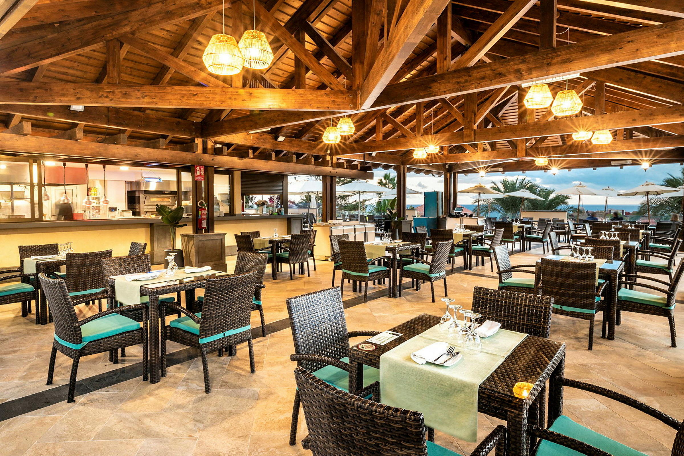 En restaurant med bord og stoler, åpen takkonstruksjon og utsikt mot en terrasse. (AI-generert tekst)