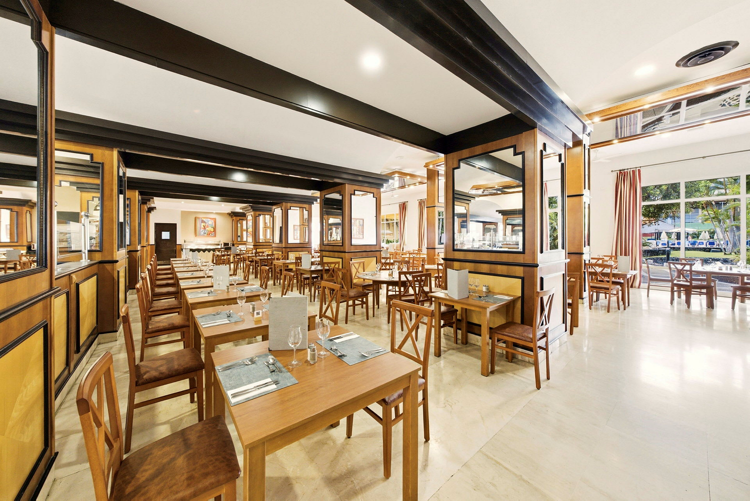 En romslig restaurant med trebord og stoler, lys interiør og vinduer med utsikt mot trær. (AI-generert tekst)