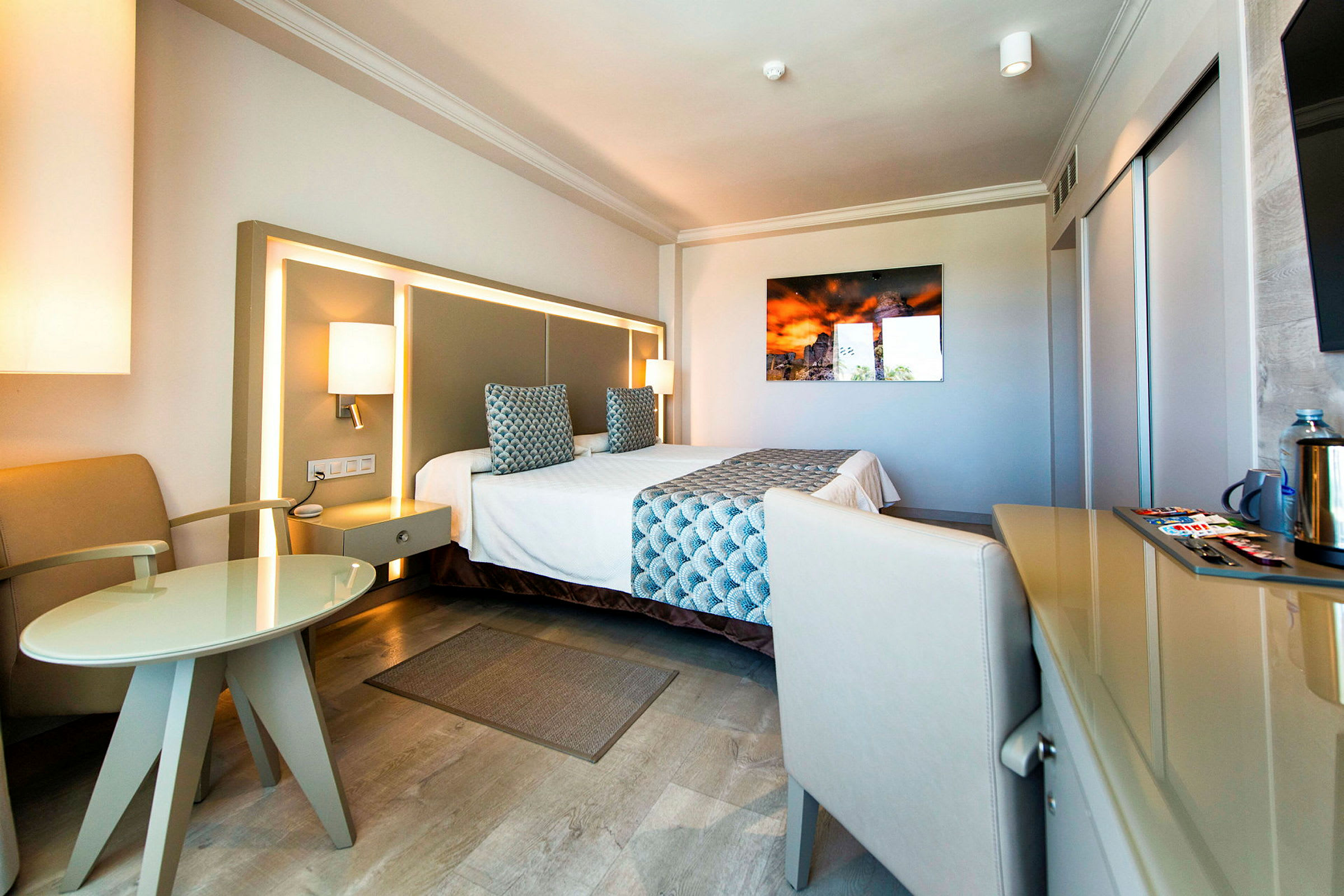 Hotellrom med en dobbeltseng, lenestol, bord og moderne interiørdetaljer. (AI-generert tekst)