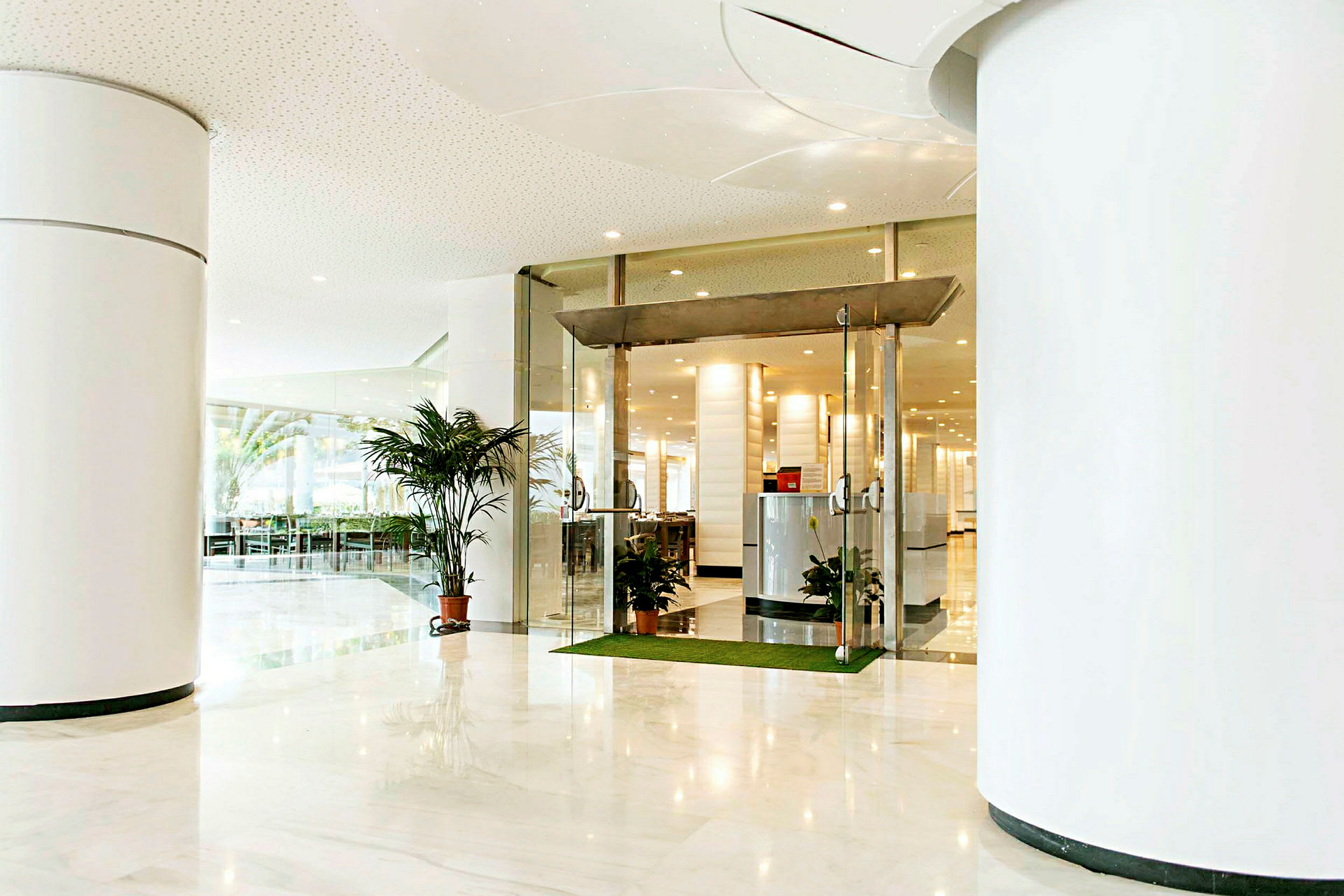 Lys hotellobby med glassdører og planter. (AI-generert tekst)
