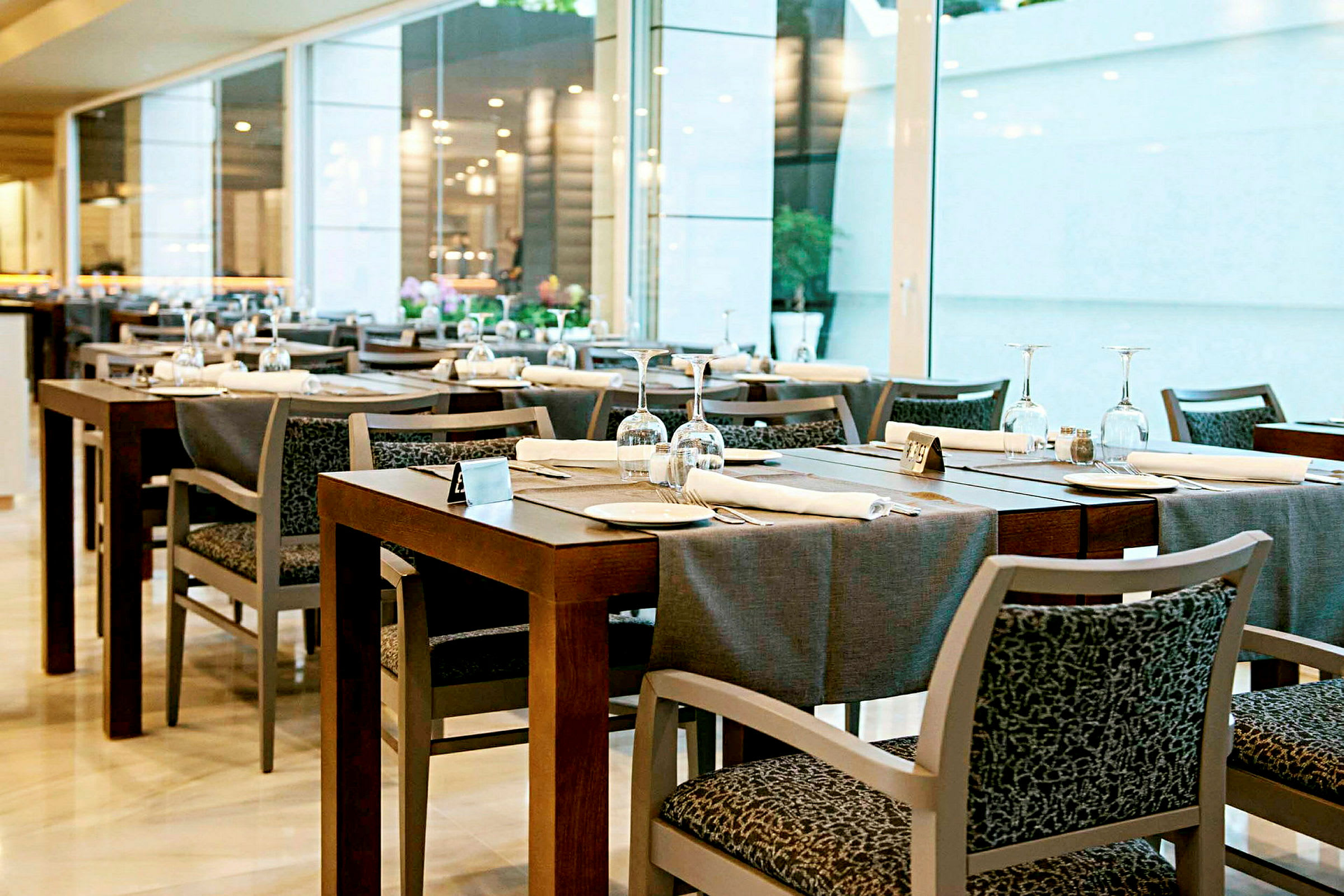 Spisebord med duker, glass og tallerkener i et moderne restaurantmiljø. (AI-generert tekst)