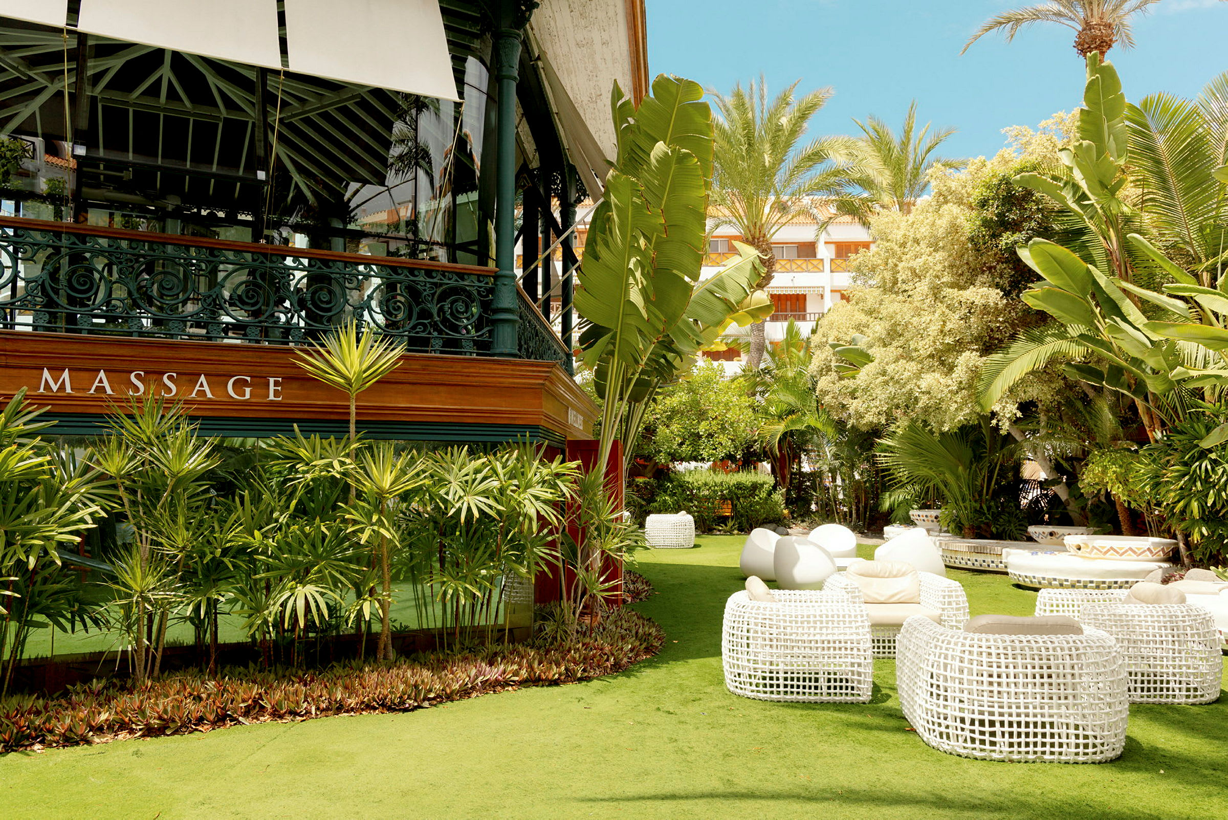 En frodig hage med hvite rottingmøbler og massasjesenter. (AI-generert tekst)