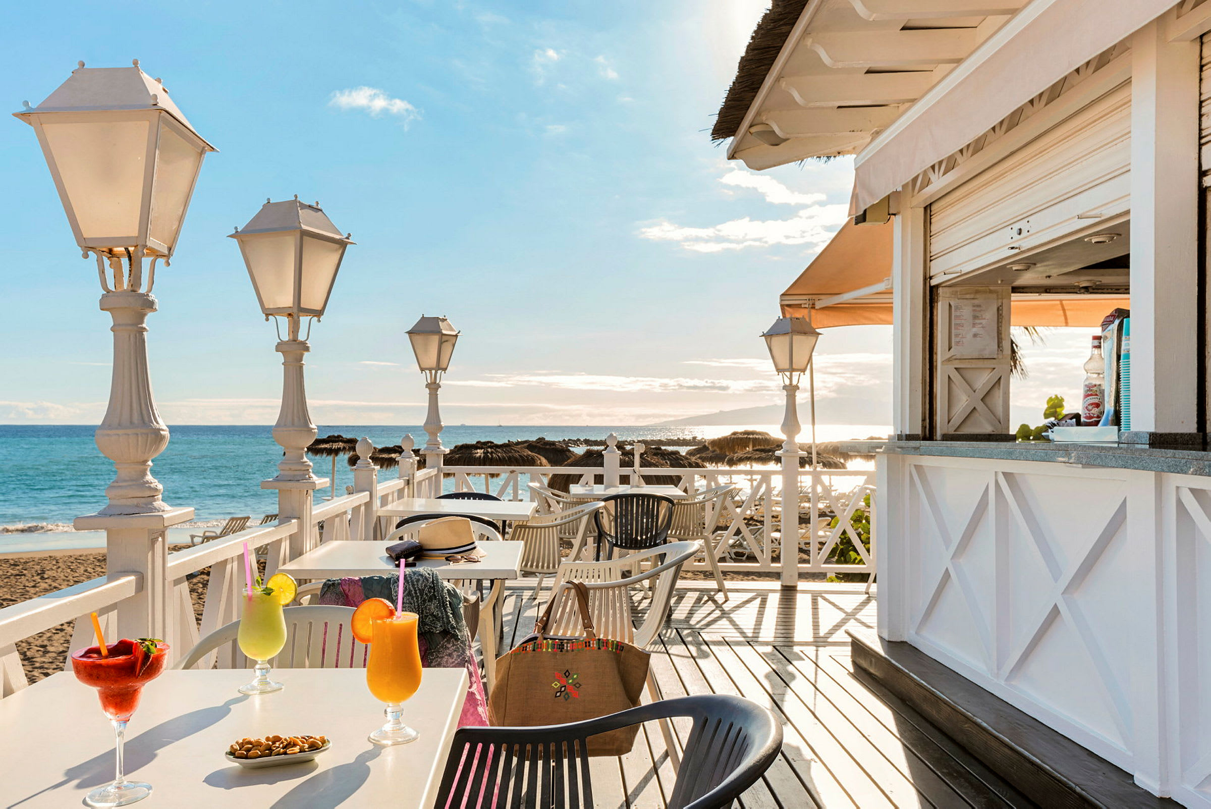 En strandkafé med bord, drikke og utsikt over havet. (AI-generert tekst)
