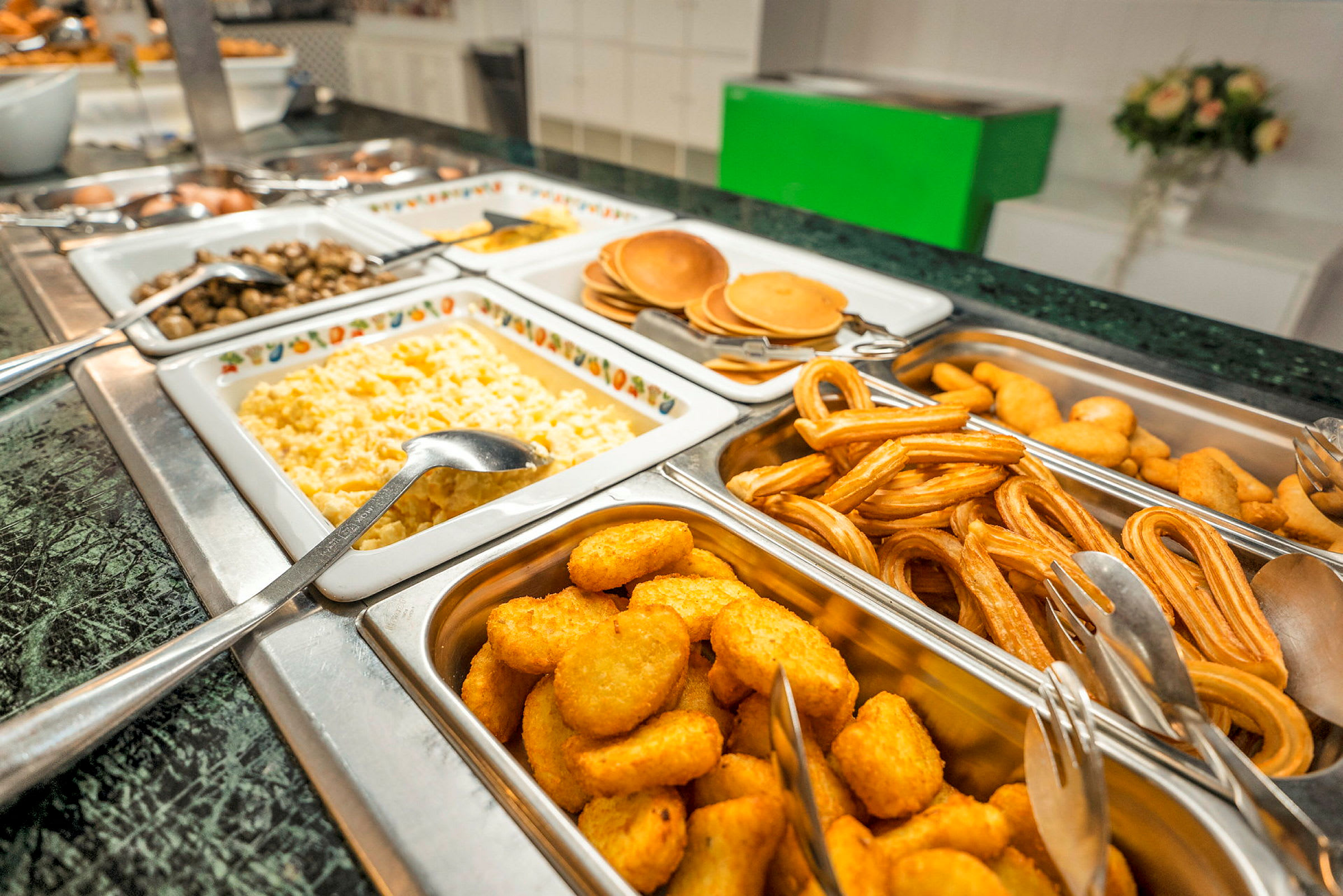 Bilde av en buffé som er fylt med forskjellige retter, inkludert eggerøre, pannekaker, churros og sprø nuggets. (AI-generert tekst)