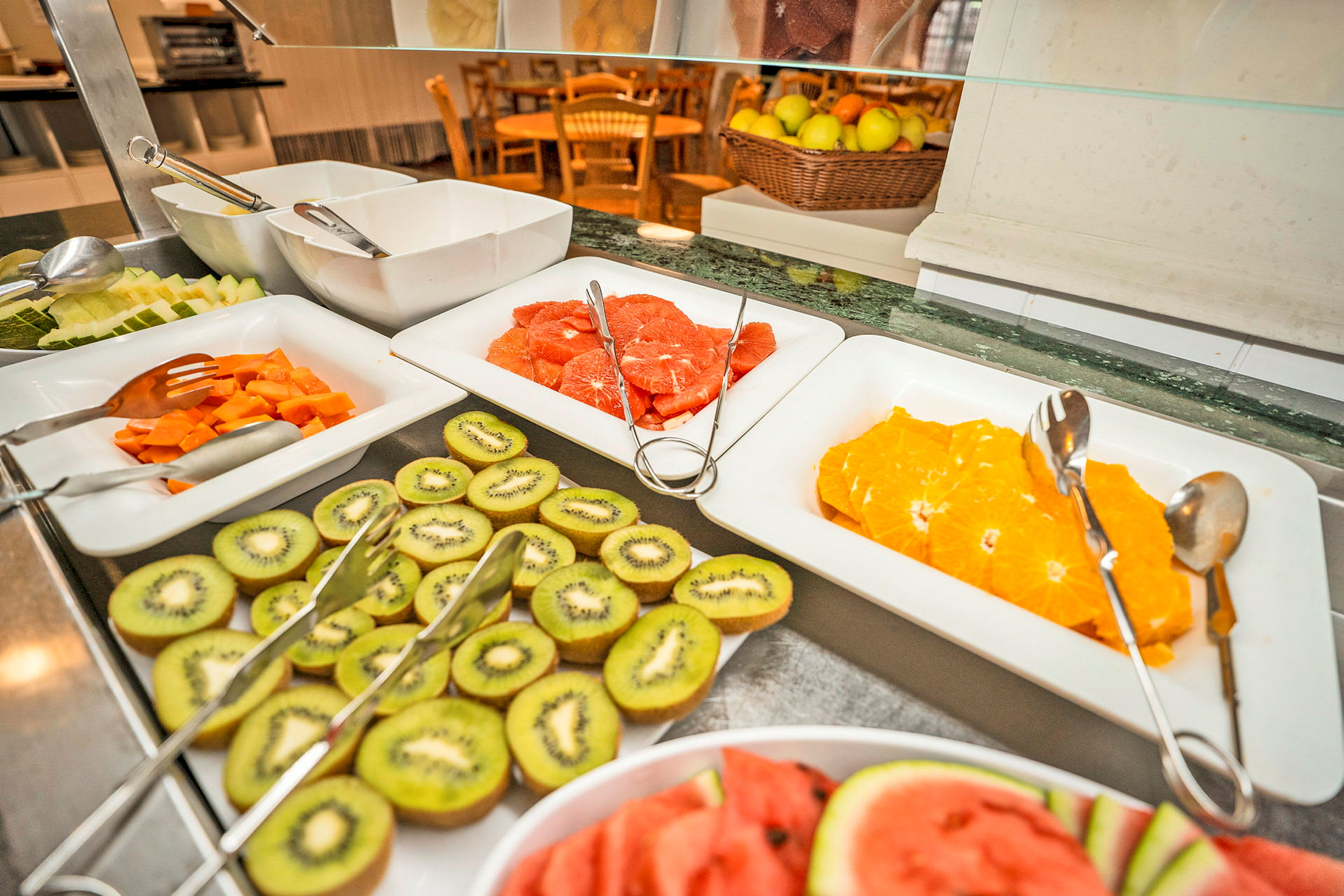 Buffetbord med oppskåret frukt som appelsiner, kiwi og vannmelon i fat. (AI-generert tekst)