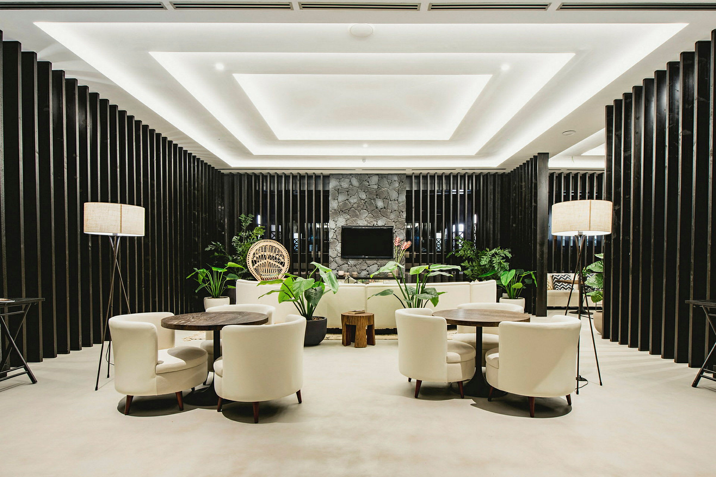 Et moderne rom med sofaer, bord og stoler arrangert sammen med grønne planter og stilfull belysning. (AI-generert tekst)