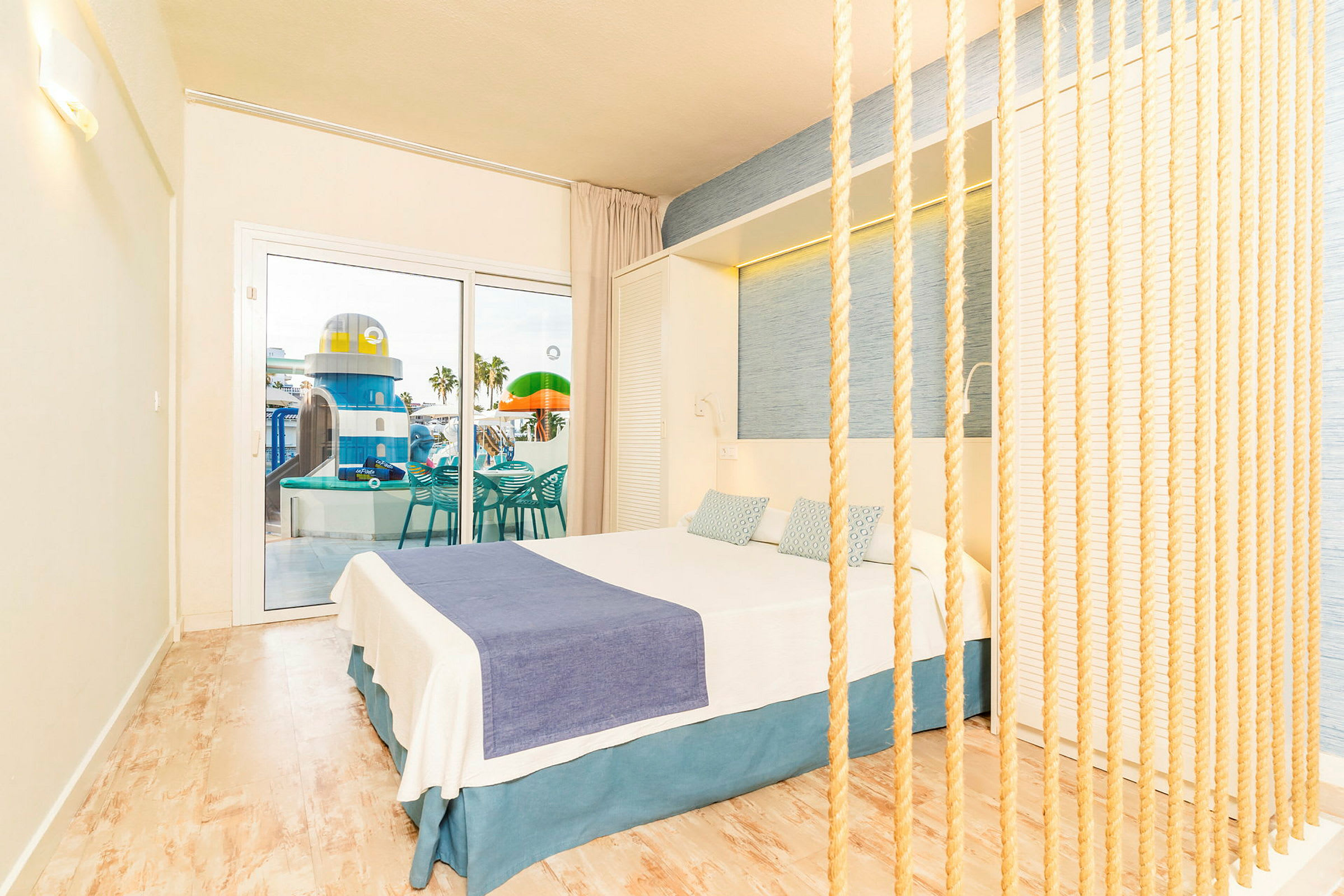 Hotellrom med lys innredning og utsikt mot et basseng og lekeplass. (AI-generert tekst)