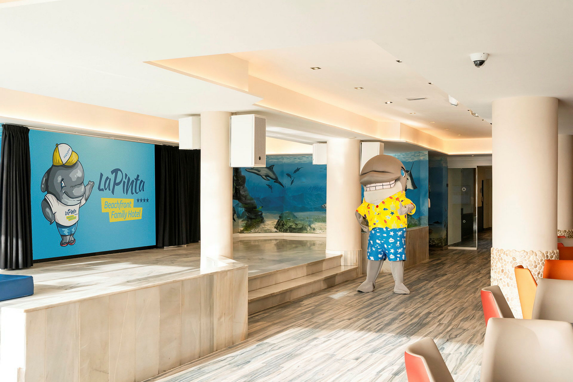 En hotellinteriør med et akvariumvegg og en delfinmaskot. (AI-generert tekst)