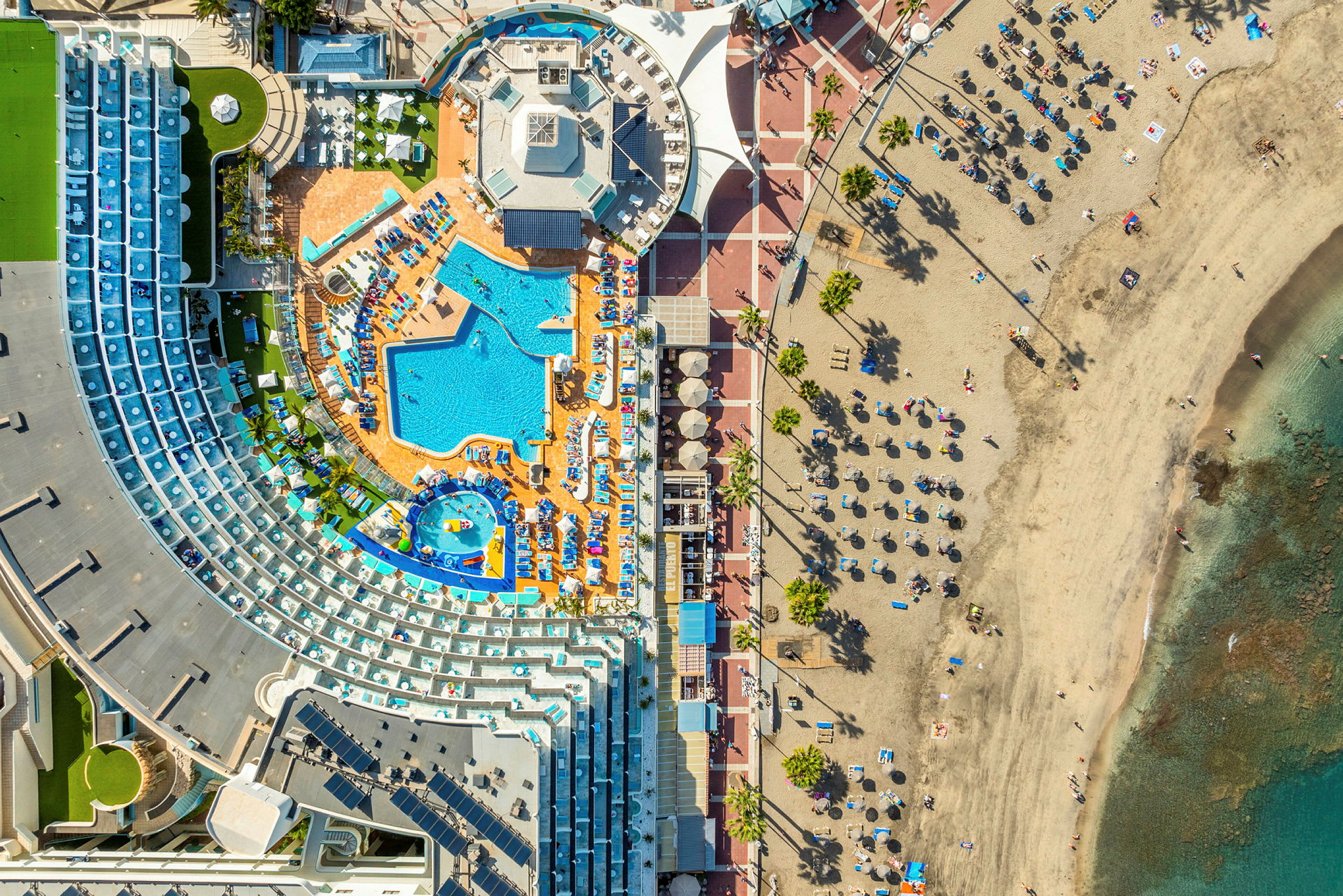 Flyfoto av hotellområde med basseng og strand. (AI-generert tekst)