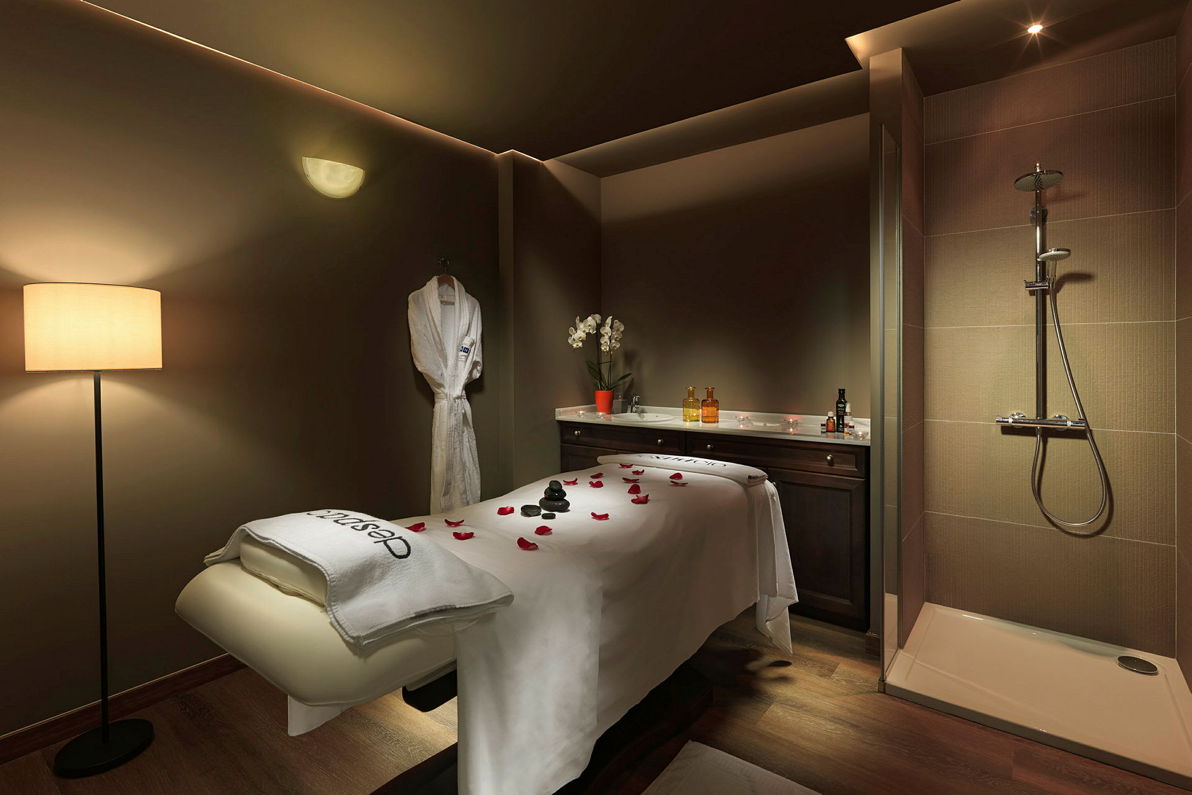 Et rom for spa- eller massasje med en behandlingsbenk, en dusj og en badekåpe hengende på veggen. (AI-generert tekst)