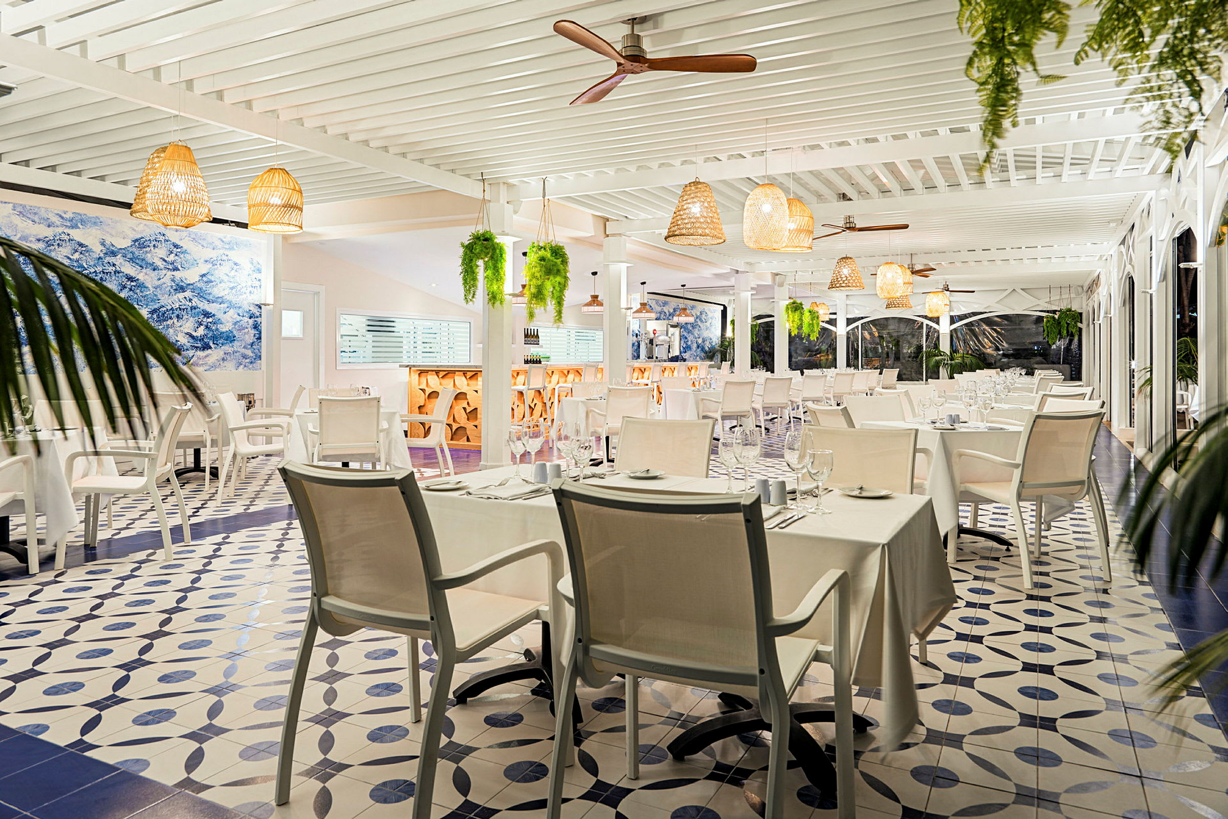 En lys restaurant med hvite duker og moderne møbler. Taklamper og planter henger fra taket. (AI-generert tekst)