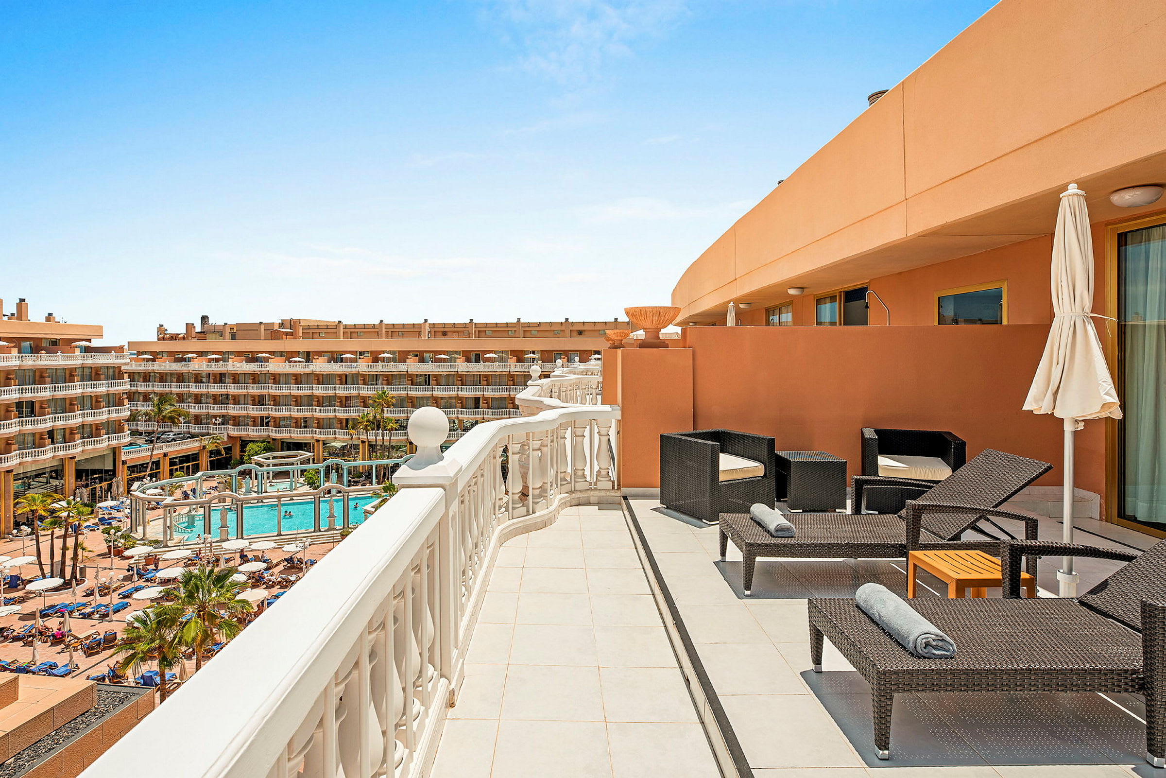 En hotellterrasse med stoler, solsenger og utsikt over bassengområdet. (AI-generert tekst)