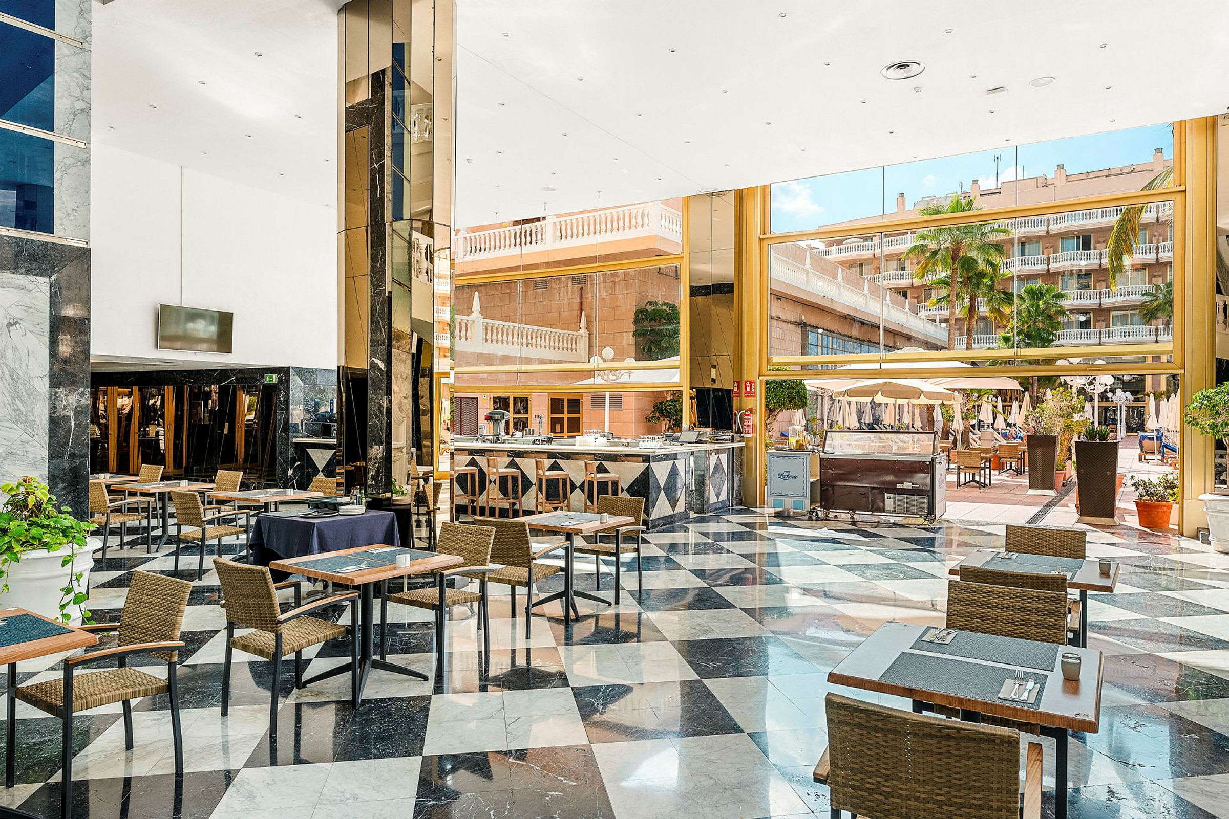 En romslig hotellobby med bord og stoler, store vinduer med utsikt over en uteplass og bassengområde. (AI-generert tekst)