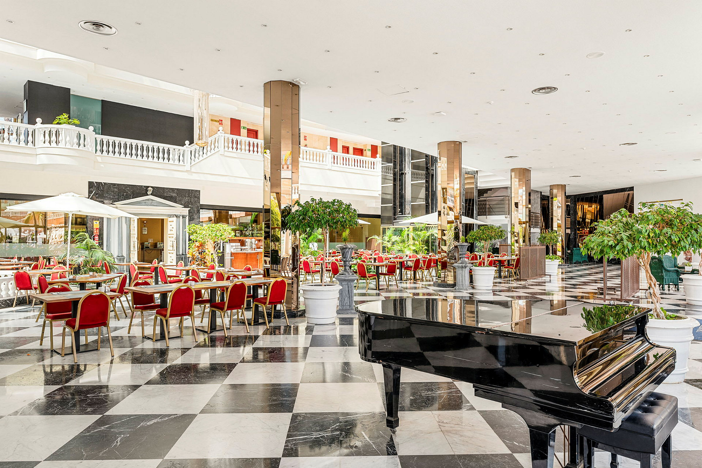 En romslig hotellobby med svart-hvitt rutete gulv, røde stoler og et svart piano. (AI-generert tekst)