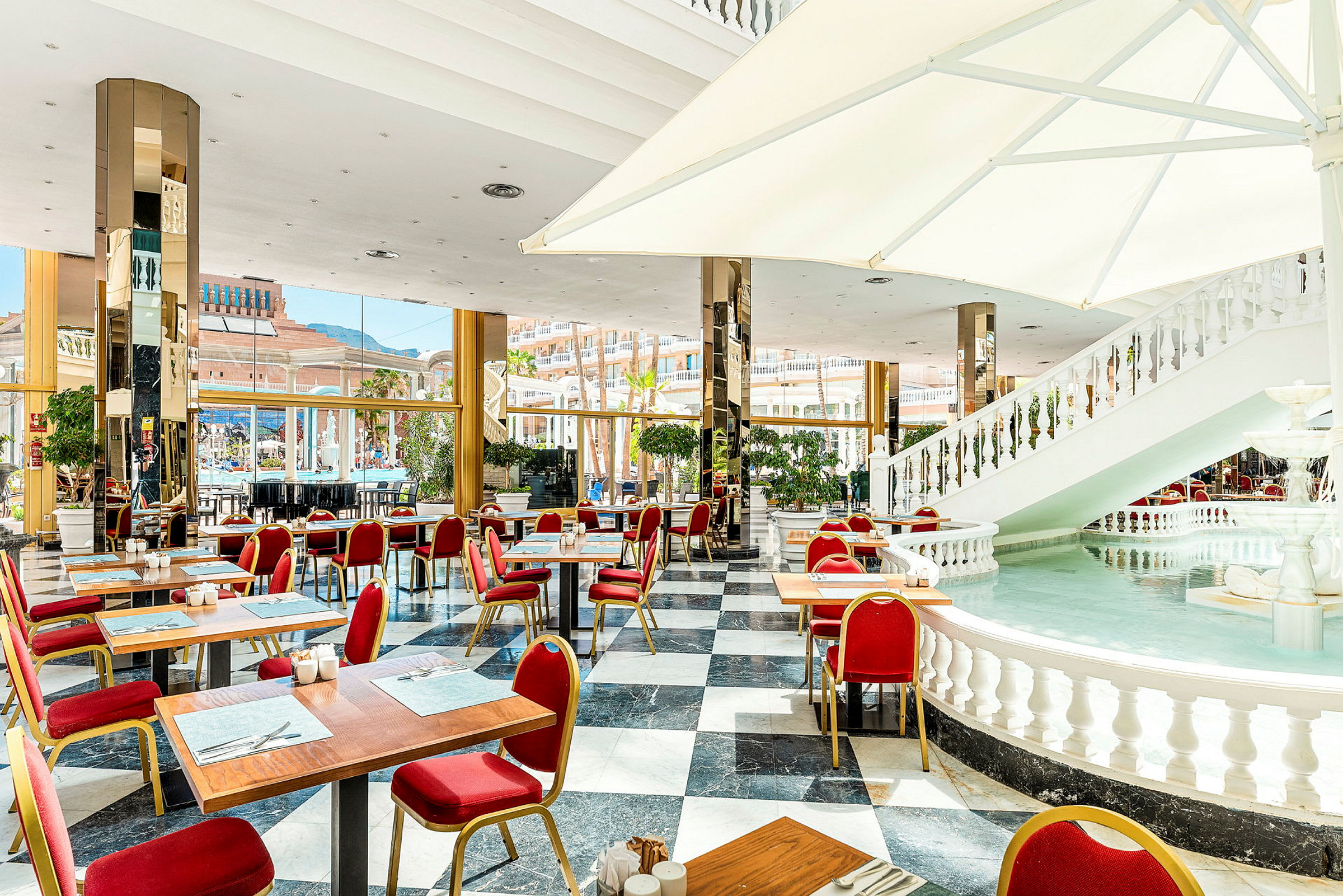 Et lyst og luftig restaurantmiljø med marmorgulv, røde stoler og innendørsfontene. (AI-generert tekst)