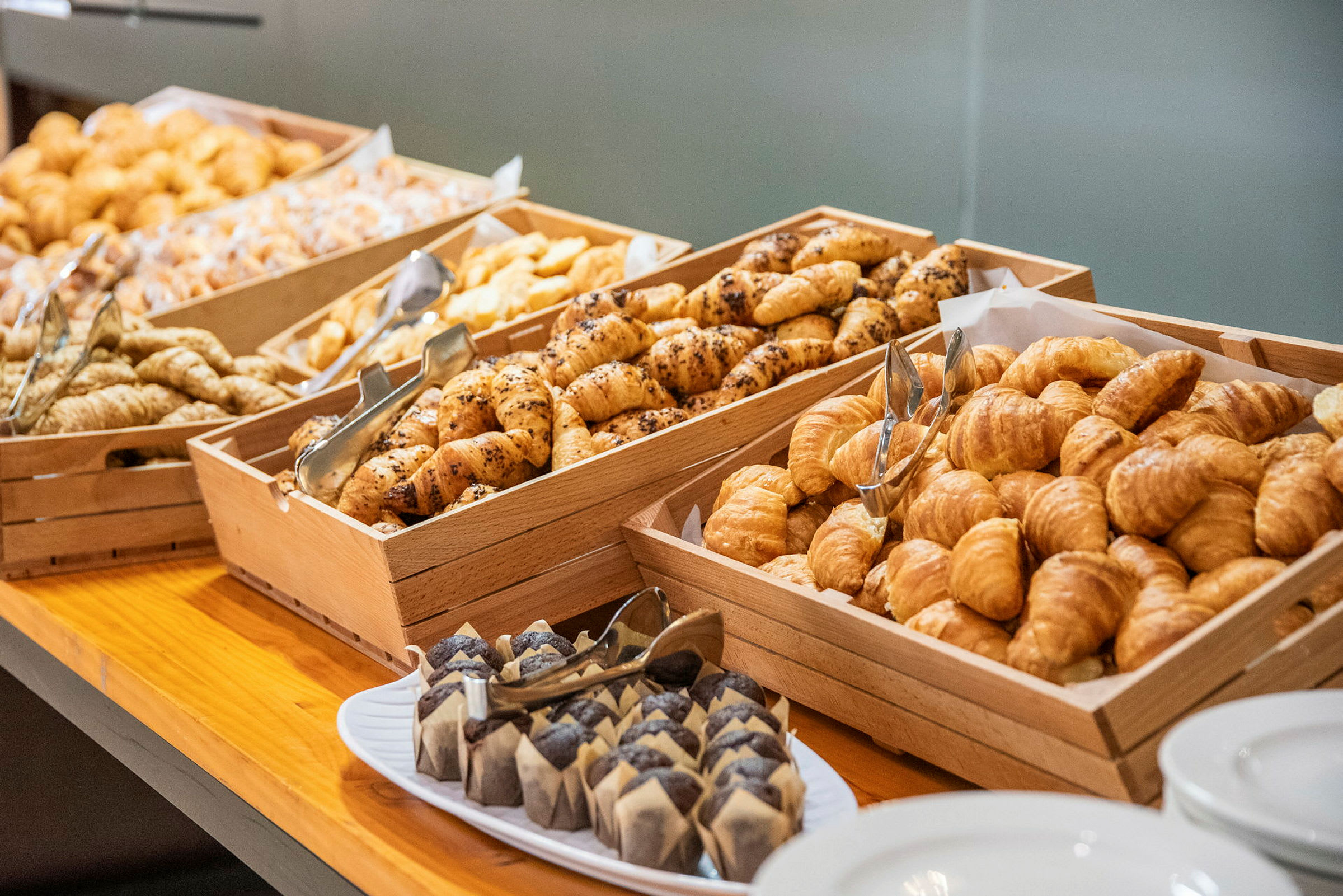 Brød og bakverk lagt opp i trekasser, samt en tallerken med muffins på et bord. (AI-generert tekst)