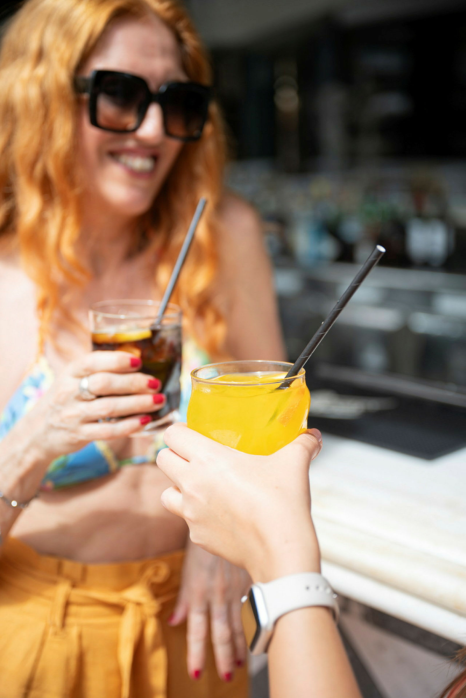 To personer som løfter glassene sine i en skål. Den ene personen holder et glass med en oransje drikk, mens den andre har et mørkere glass, begge med sugerør. (AI-generert tekst)