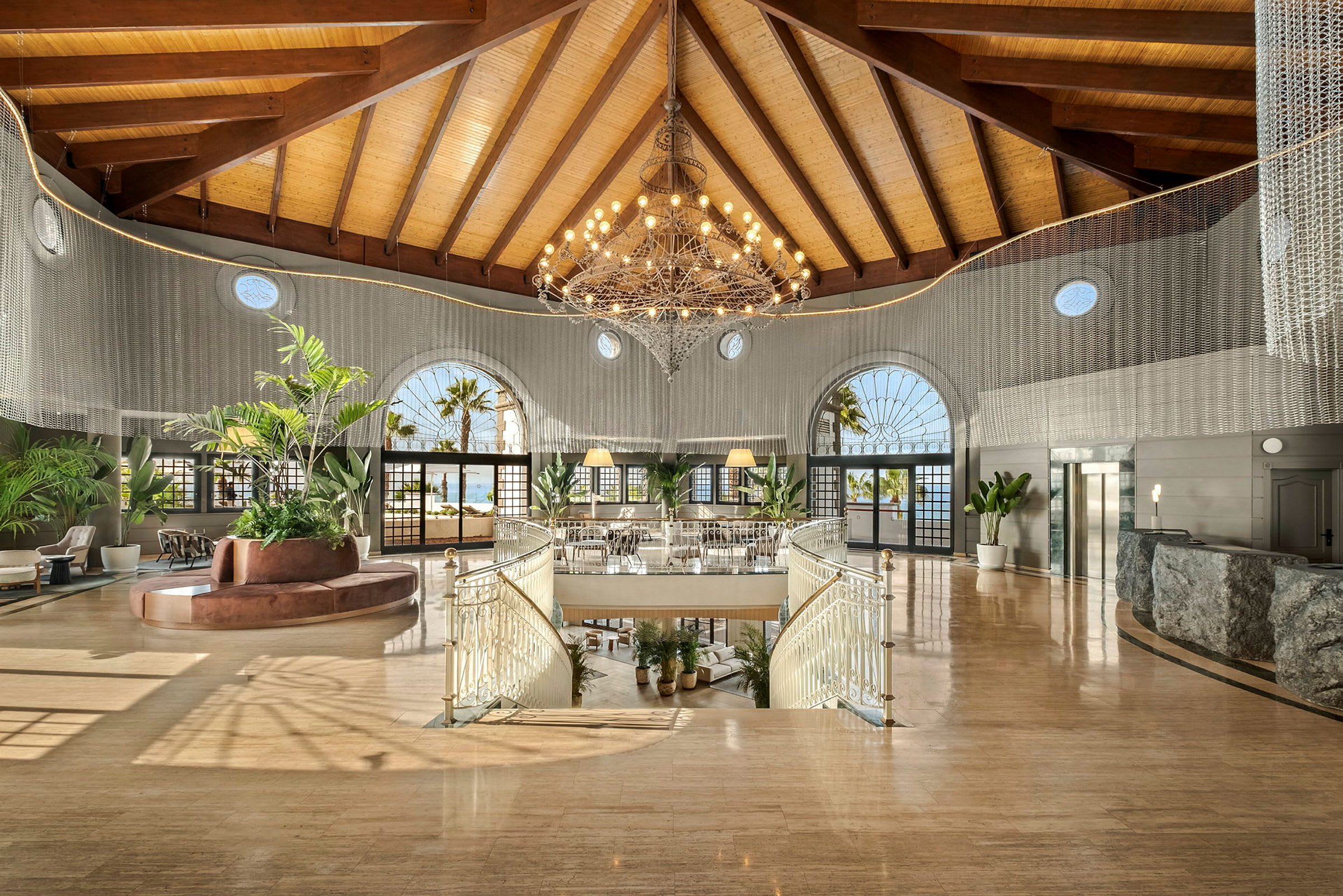Bilde av et hotellobbyområde med en stor lysekrone, moderne møbler og store vinduer. (AI-generert tekst)