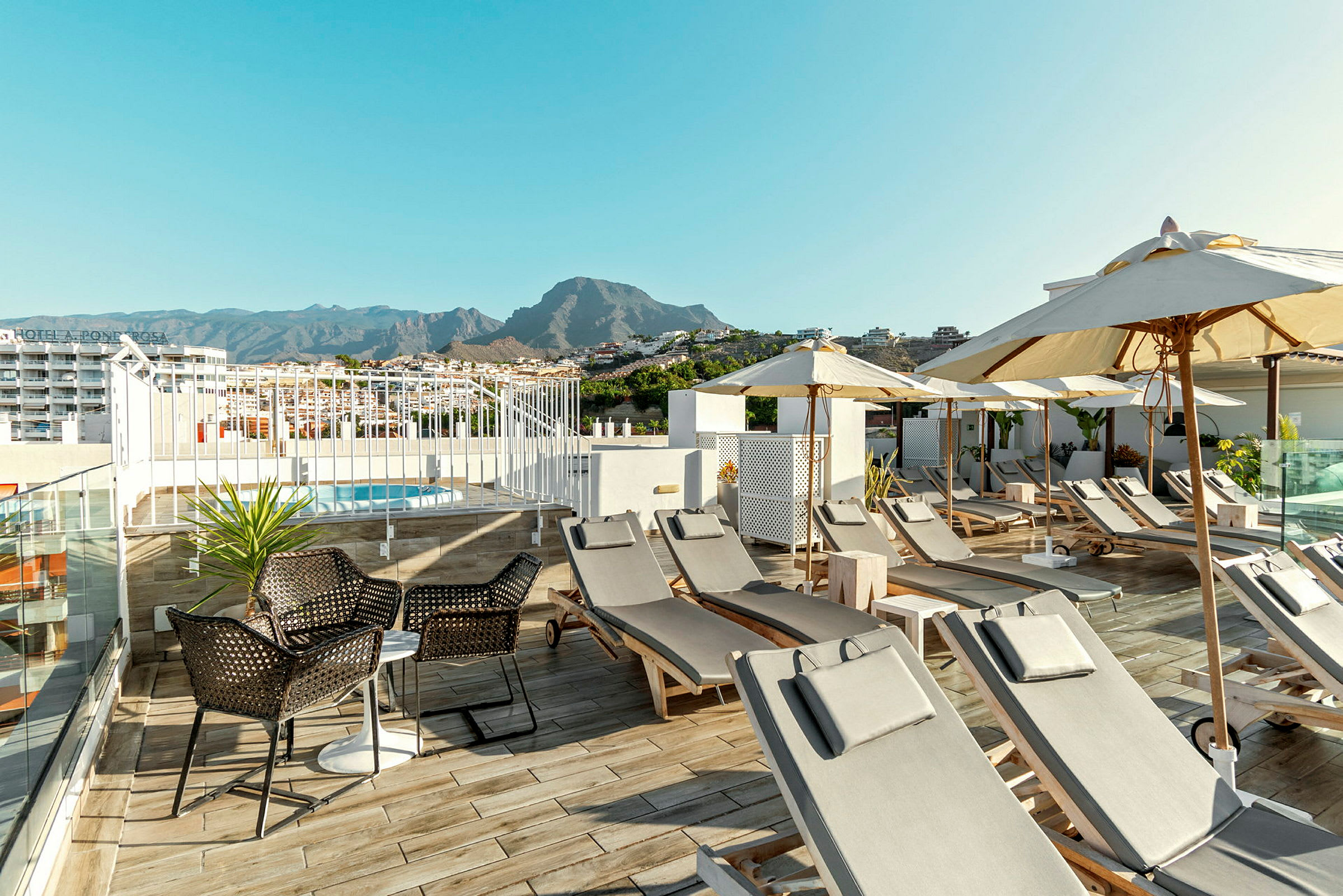 Basseng med solsenger og parasoller på en hotellt terrasse med fjell i bakgrunnen. (AI-generert tekst)
